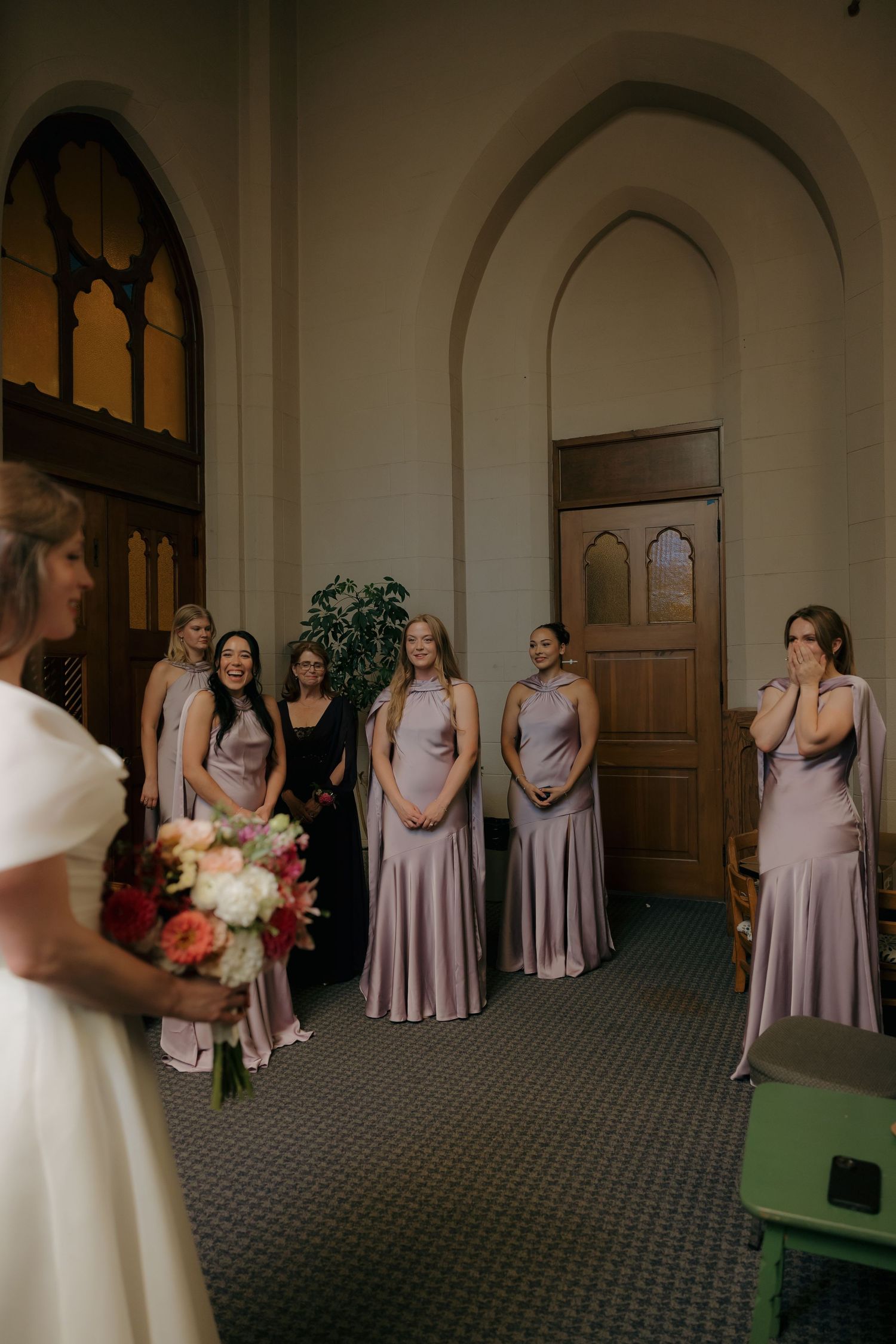 Bridesmaids in lavender gowns react emotionally seeing bride before wedding ceremony.
