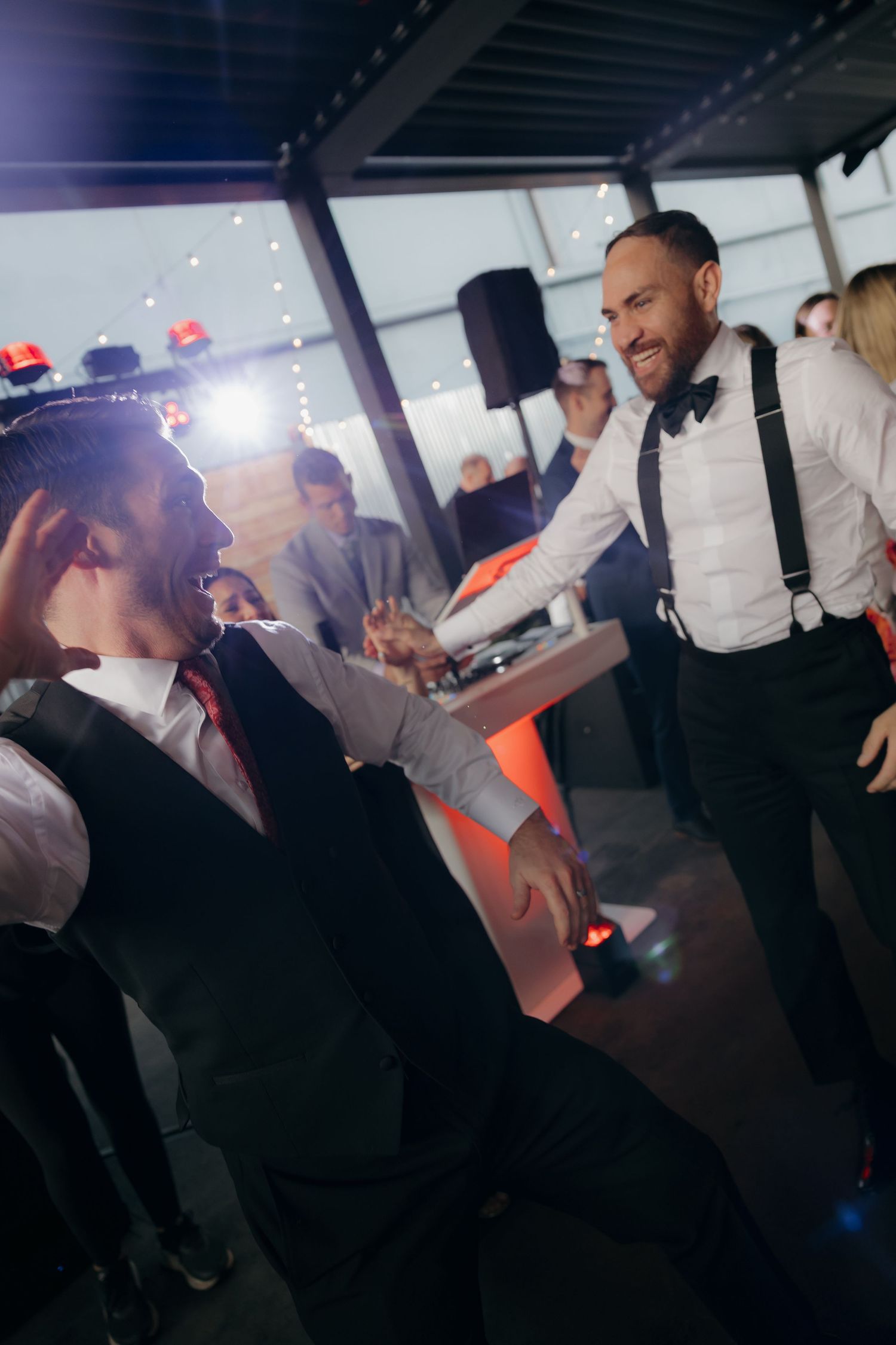 Two groomsmen laughing and dancing together at a wedding reception party.