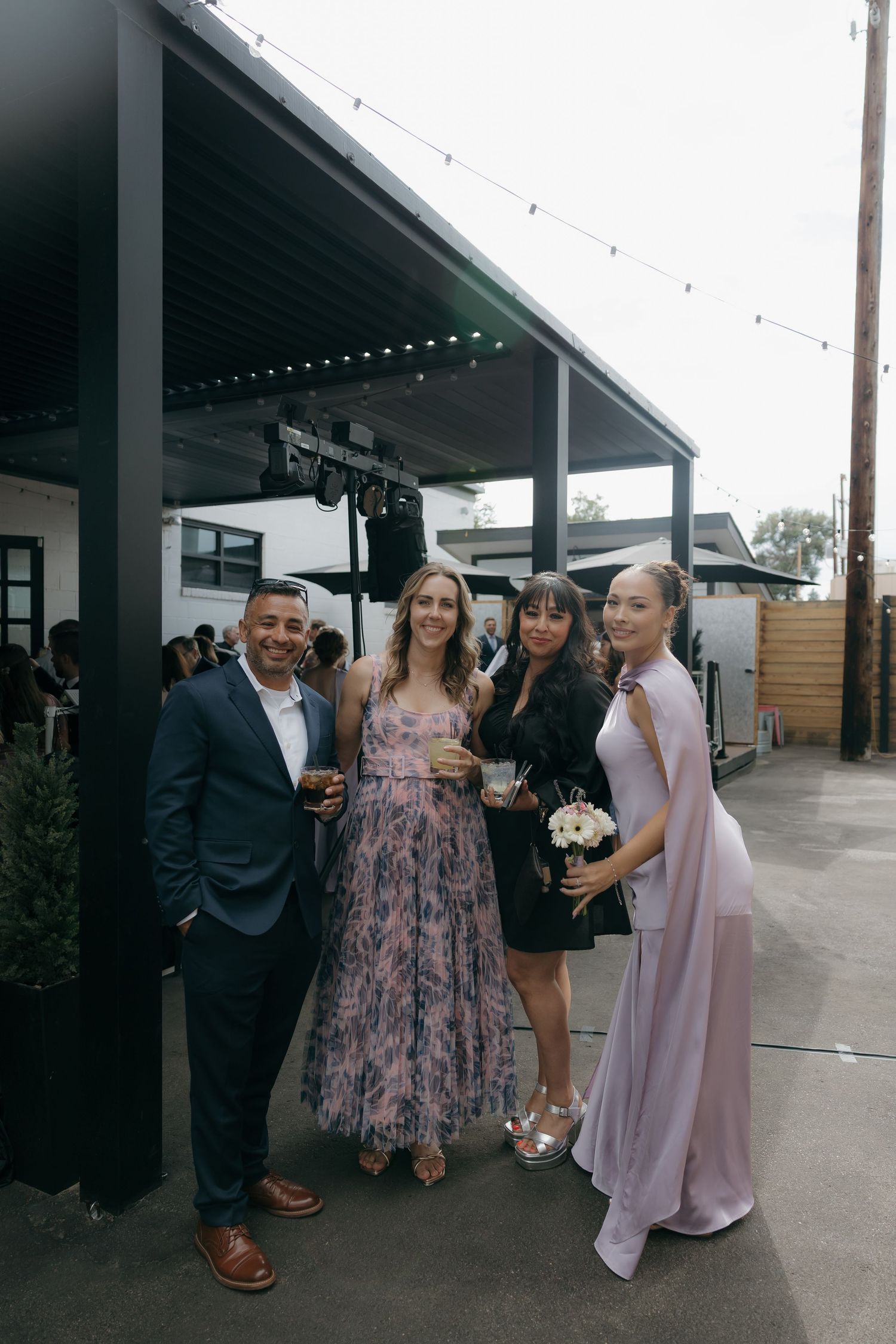 Wedding guests pose together smiling at outdoor reception venue with string lights.