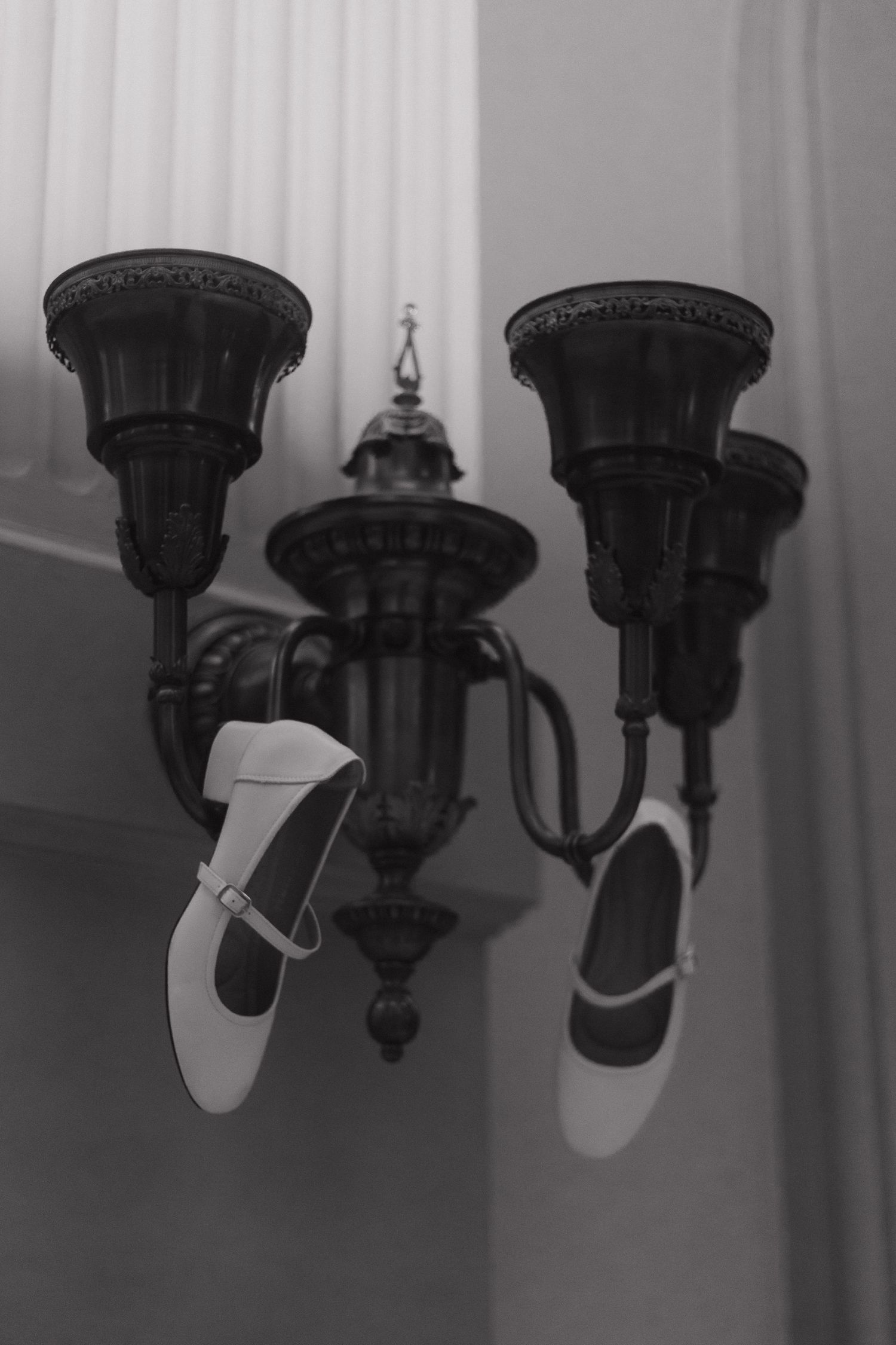 White bridal shoes hanging decoratively from an ornate vintage light fixture in black and white.