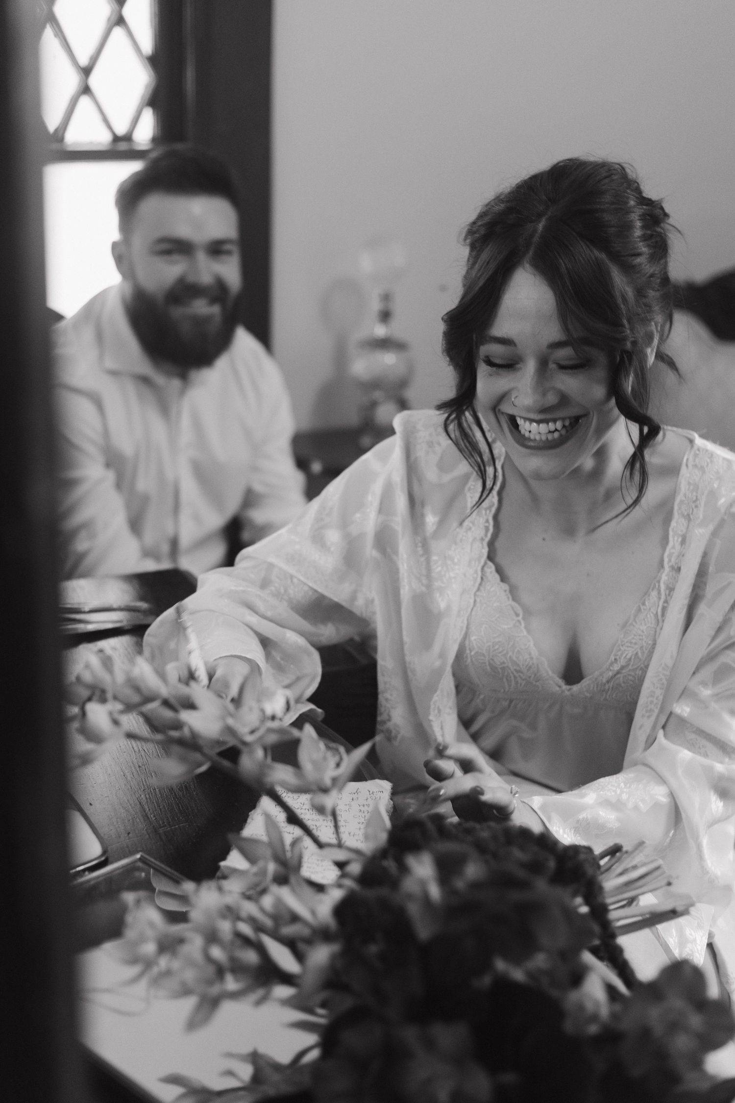 A joyful moment during wedding preparations with white robes and floral arrangements.