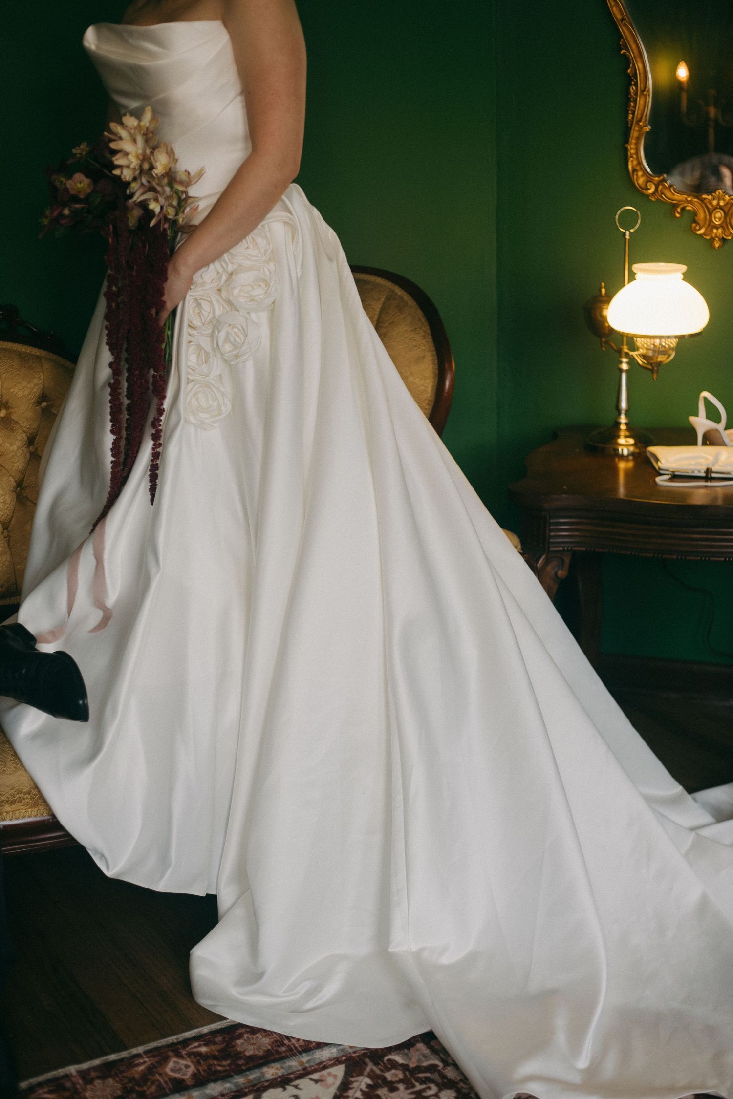 Wedding dress details showing full skirt and train against dark green walls with gold accents.