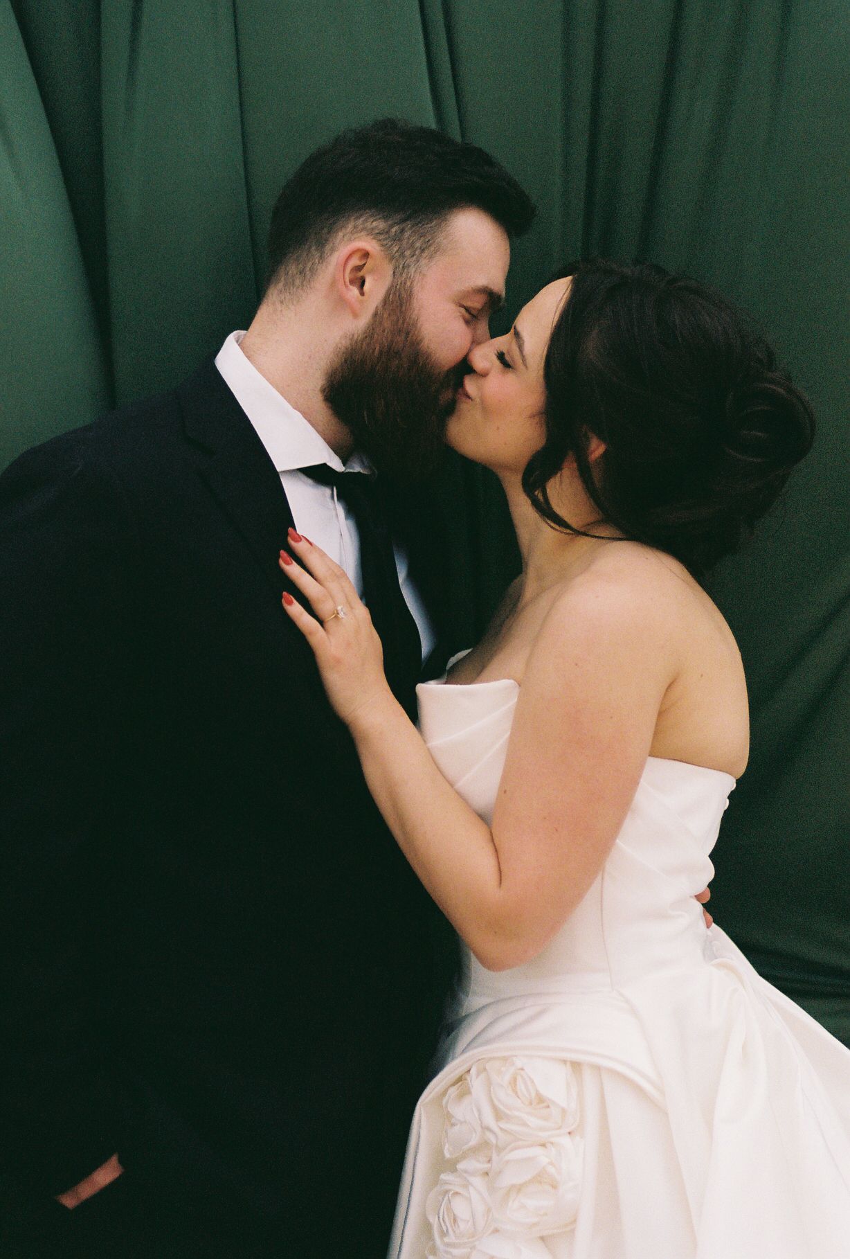 A couple in formal wedding attire share an intimate dance against a dark green backdrop.