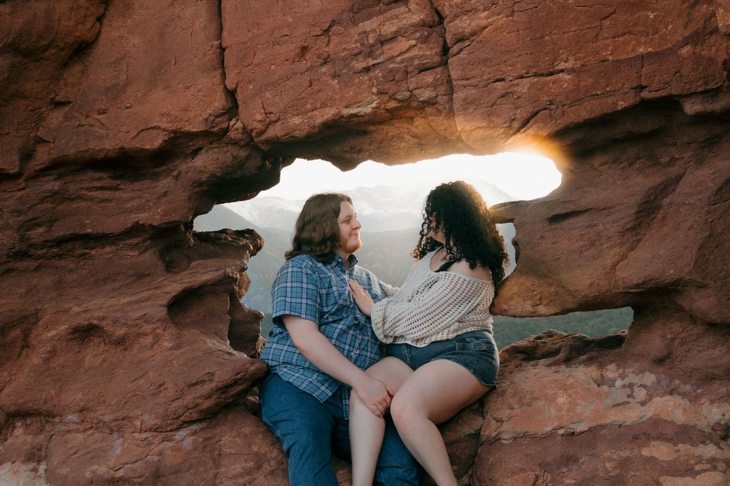 A couple sits together inside a natural rock formation cave with sunlight streaming through.