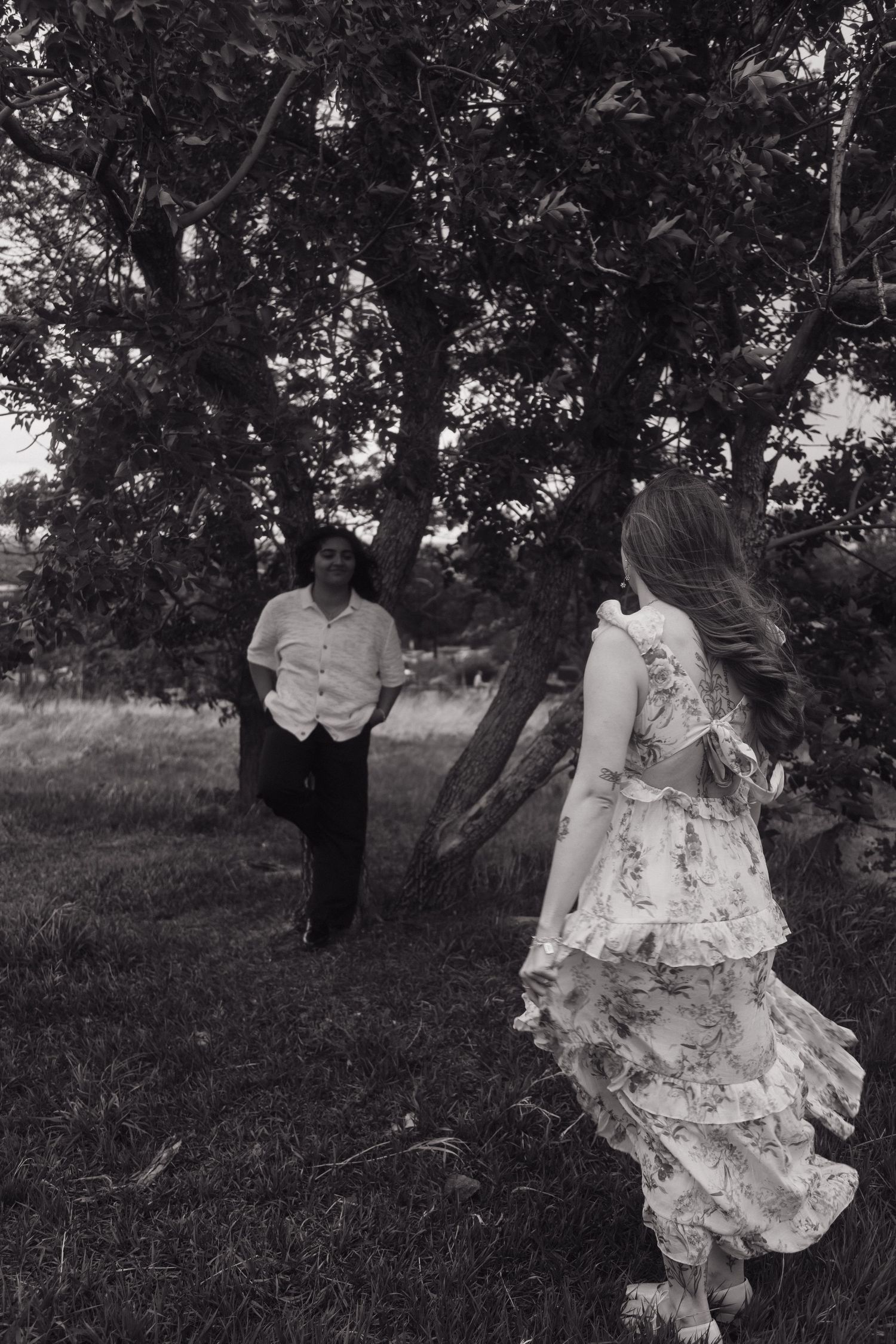 Black and white photo of couple running toward each other under a tree in a grassy field.