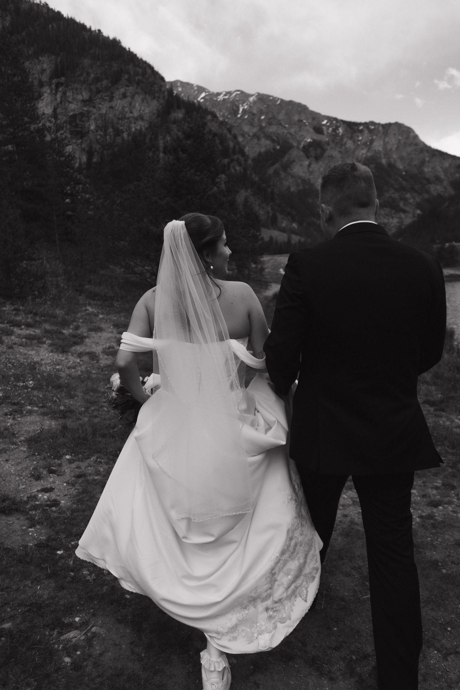 Black and white photo of bride and groom walking toward dramatic mountain landscape during their elopement.