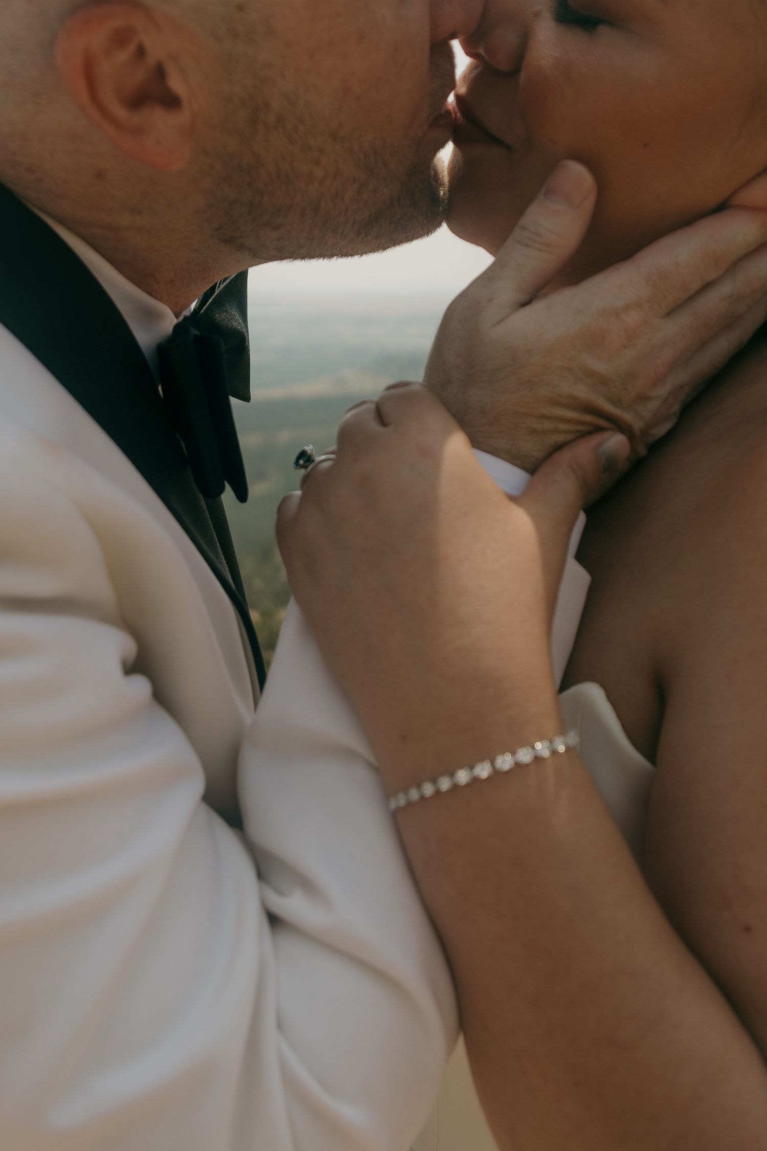 Newlyweds share first kiss with bride wearing diamond bracelet and ring at scenic outdoor wedding.