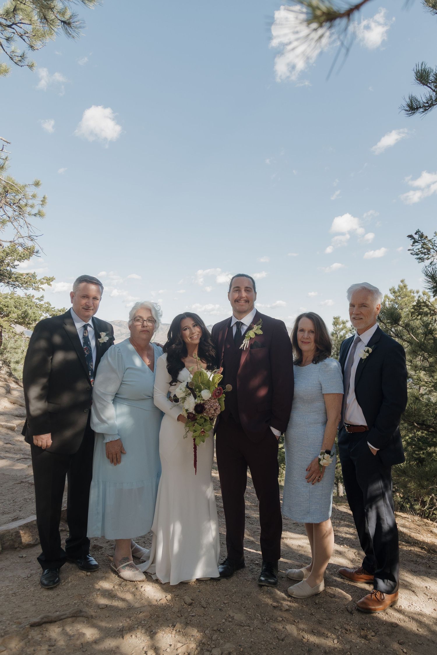 Wedding party family portrait with bride and groom outdoors against blue sky in Colorado mountains.