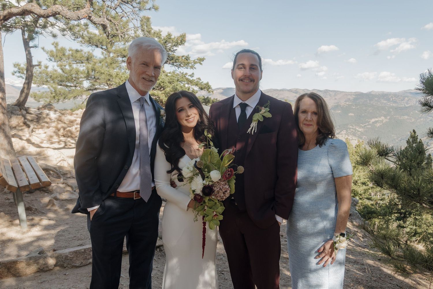Wedding party of four posing outdoors on a rocky mountain overlook with pine trees.