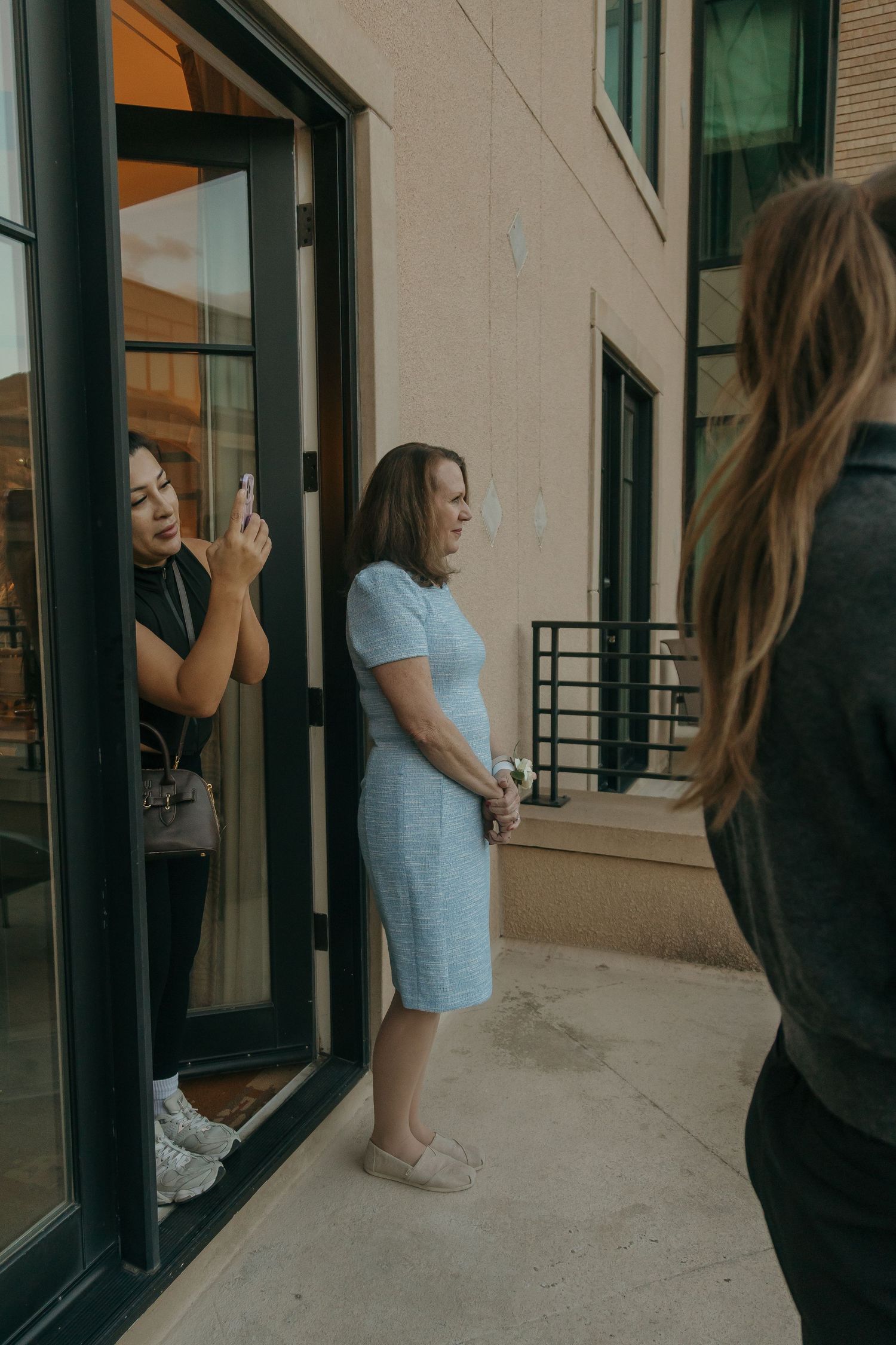 Woman in light blue dress being photographed outside hotel building on wedding day.