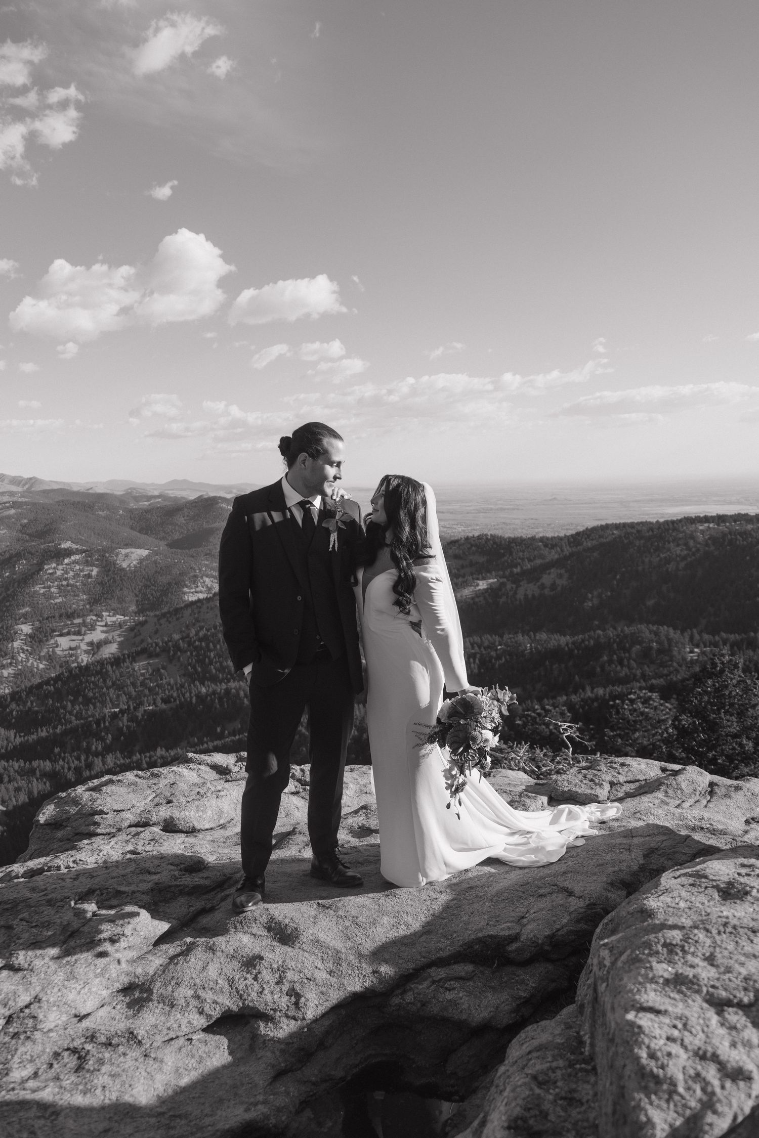 Black and white photo of bride and groom sharing a romantic moment on a mountain summit with panoramic views.