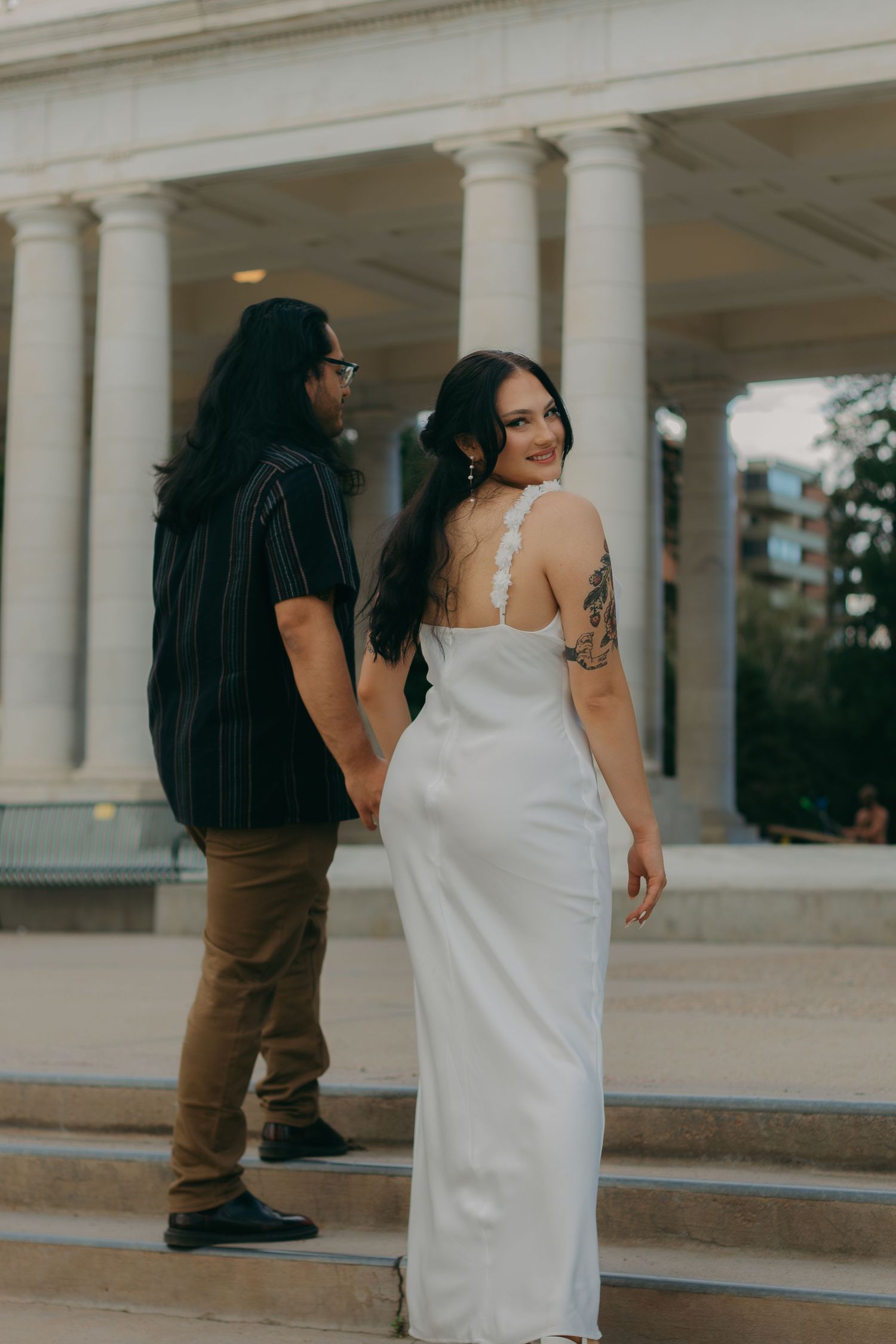 Couple posing on stone steps with classical columns in the background.