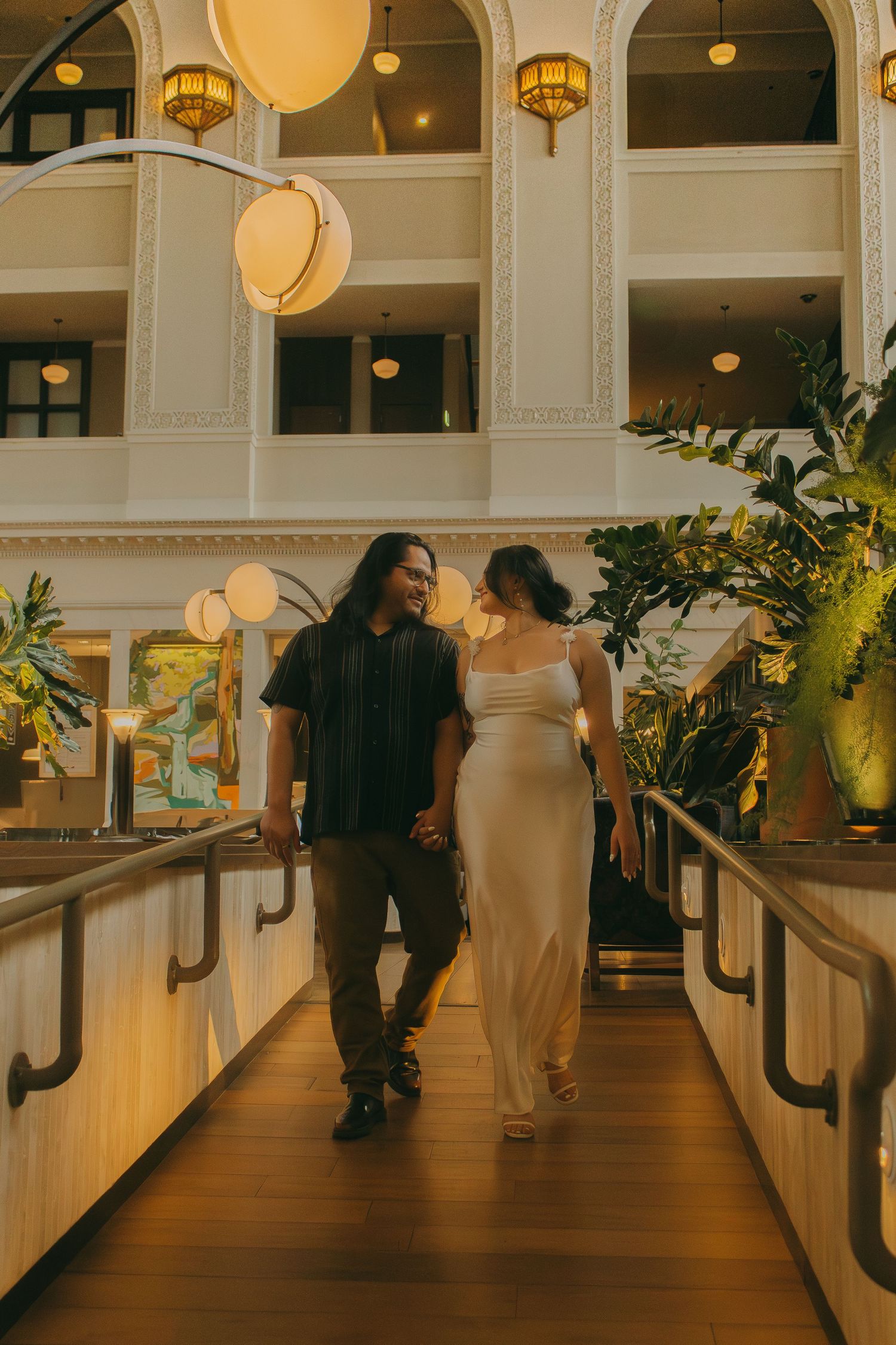 Soft yellow lighting illuminates an elegant hallway with dark wood floors and white columns creating a romantic ambiance.