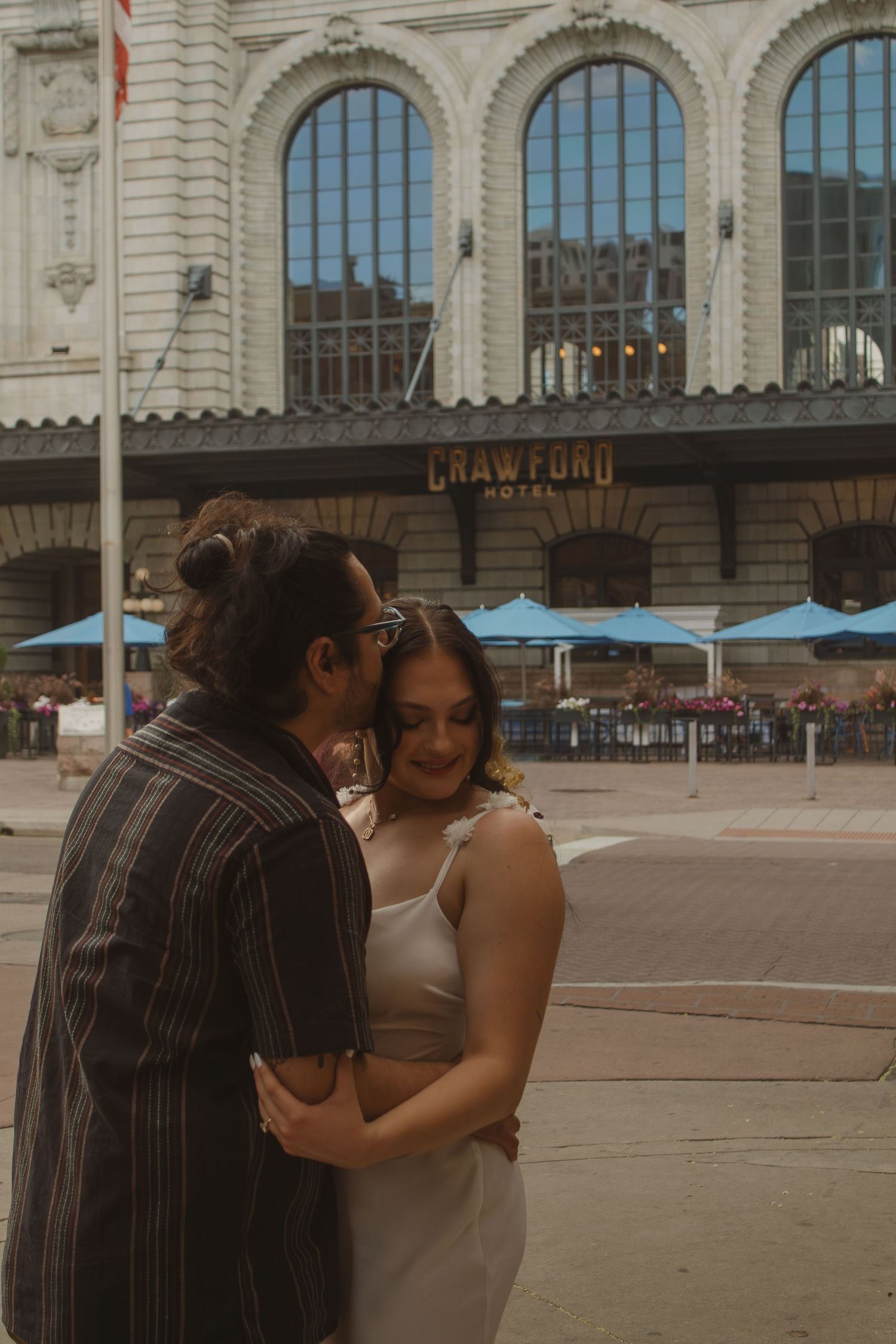 A couple embraces outside the historic Crawford building with its grand arched windows and architectural details.