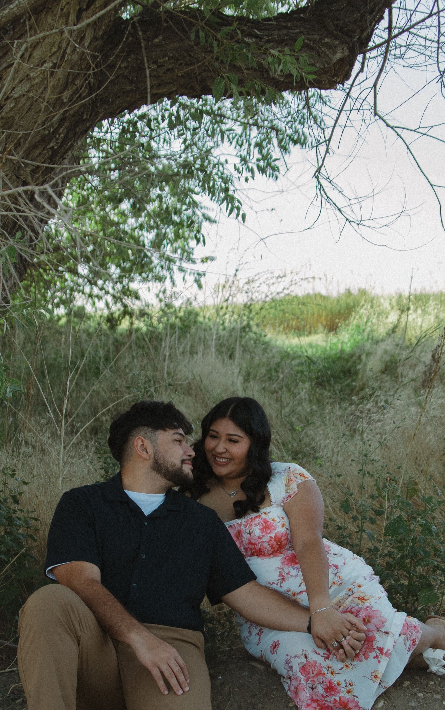 Intimate couple's photoshoot under a shady tree with natural lighting.