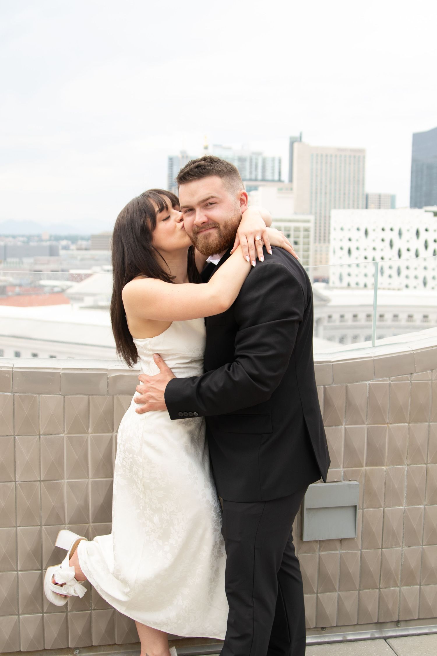 A romantic couple shares intimate moments on an urban rooftop terrace with a city skyline backdrop.