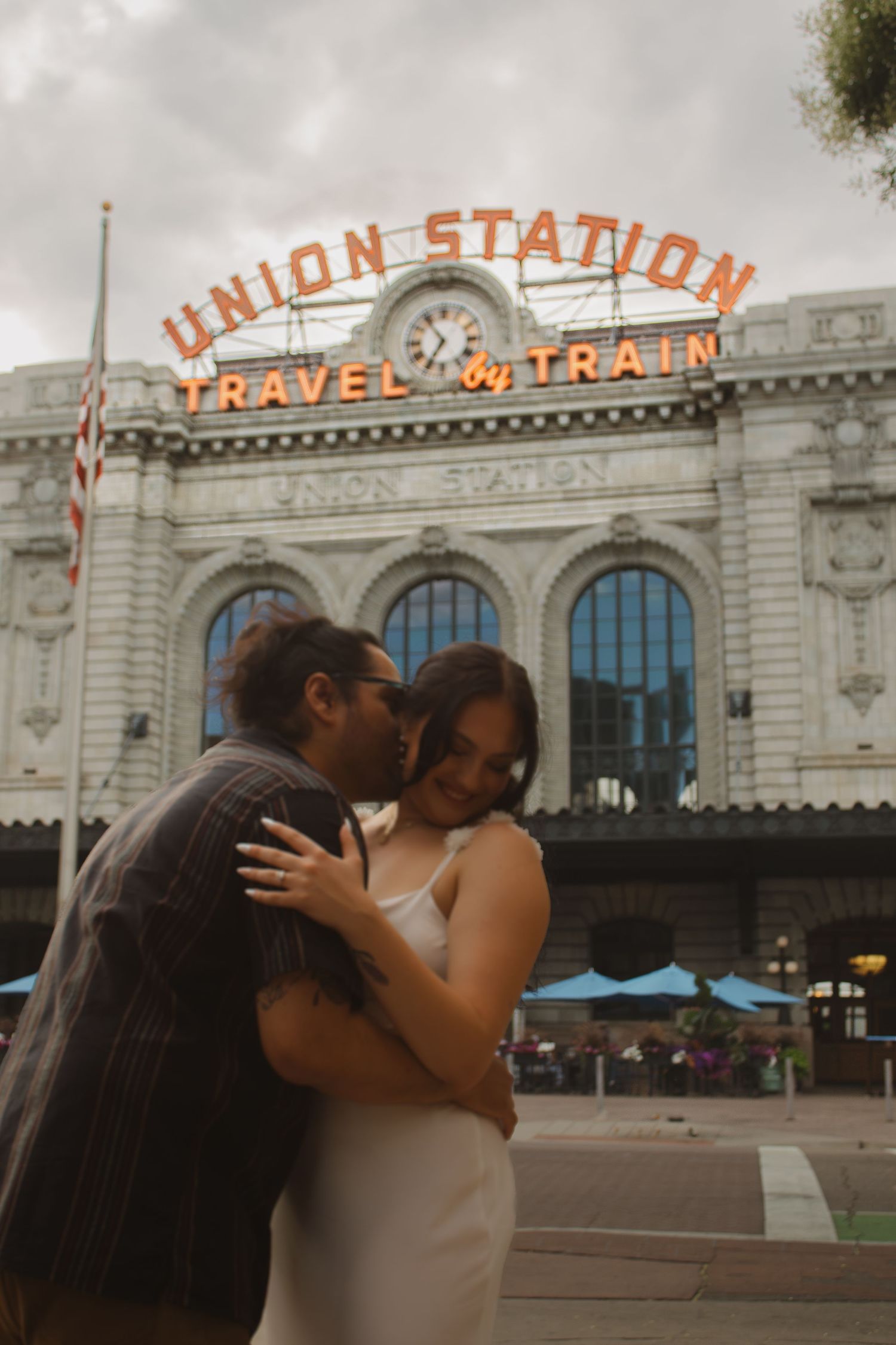 A romantic couple embraces in front of the historic Union Station Travel & Train sign in Denver.