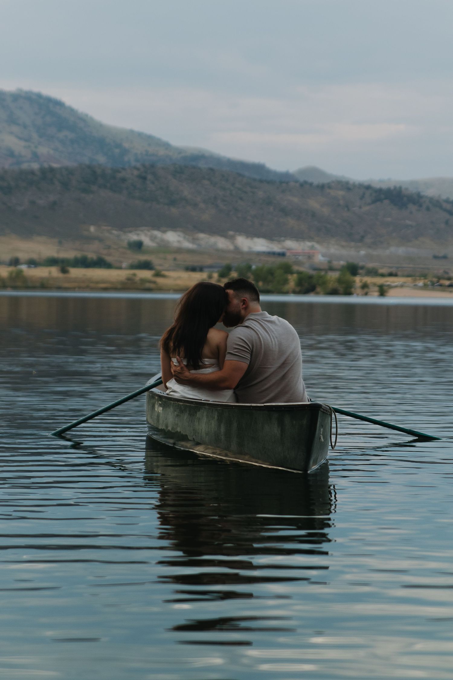 Two people rowing a small boat across serene mountain lake waters during a peaceful afternoon.