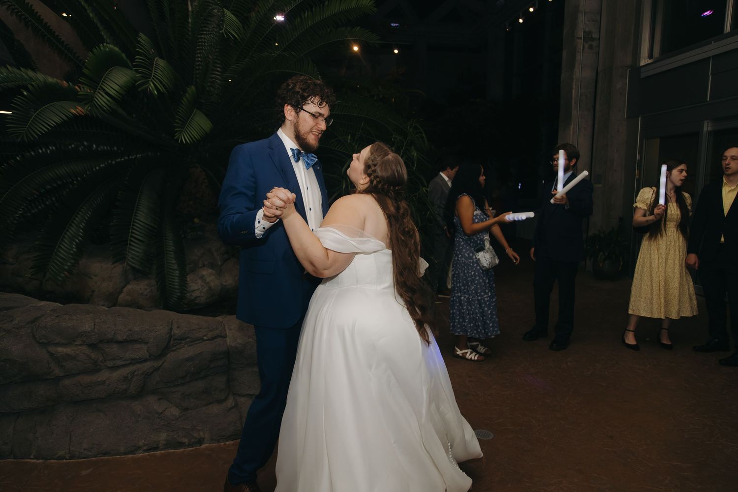 Bride and groom sharing their first dance in a tropical indoor venue surrounded by wedding guests.