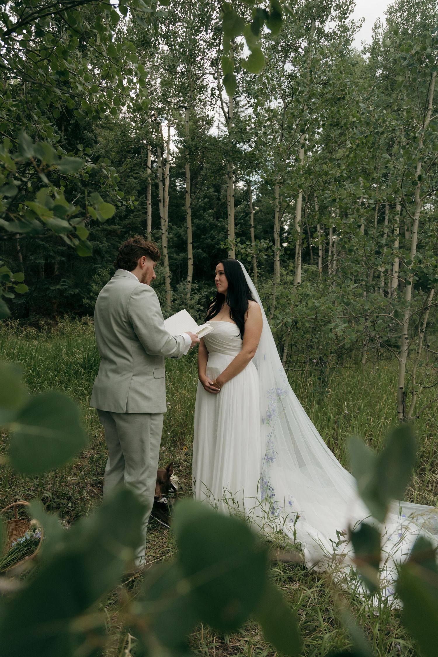 Bride and groom exchange vows among tall aspen trees in a green forest clearing during their elopement.