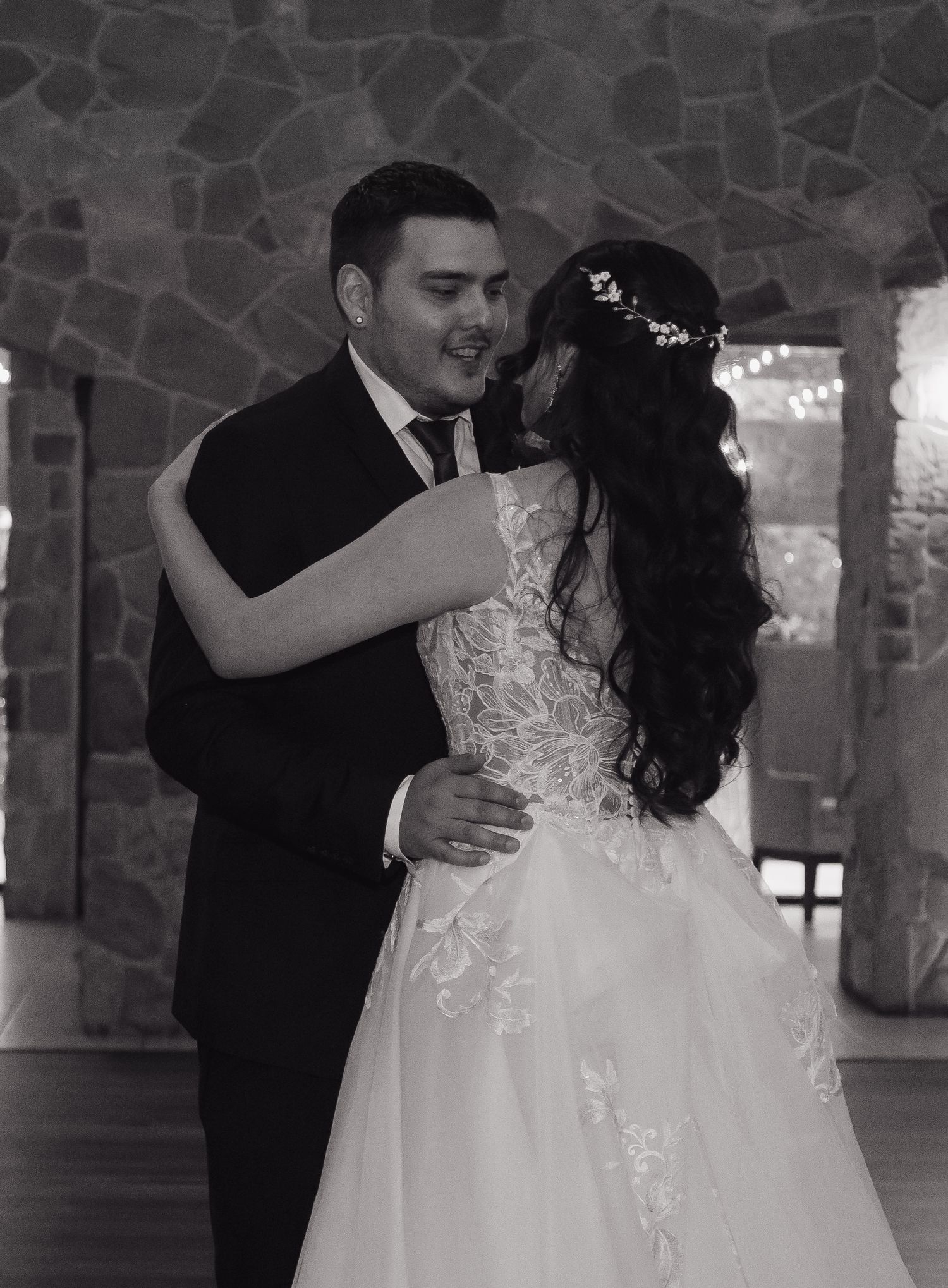 Black and white photo of bride and groom sharing romantic first dance embrace at wedding reception.