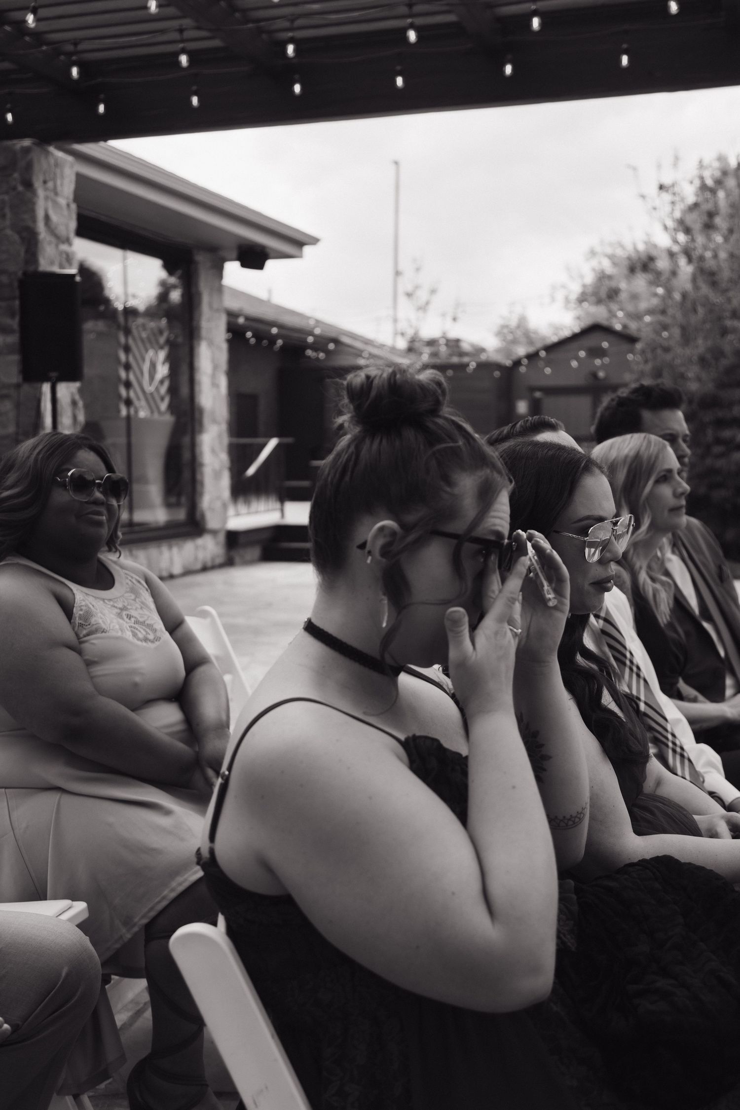 Emotional wedding guest wiping tears during outdoor ceremony while seated among other guests in black and white photo.
