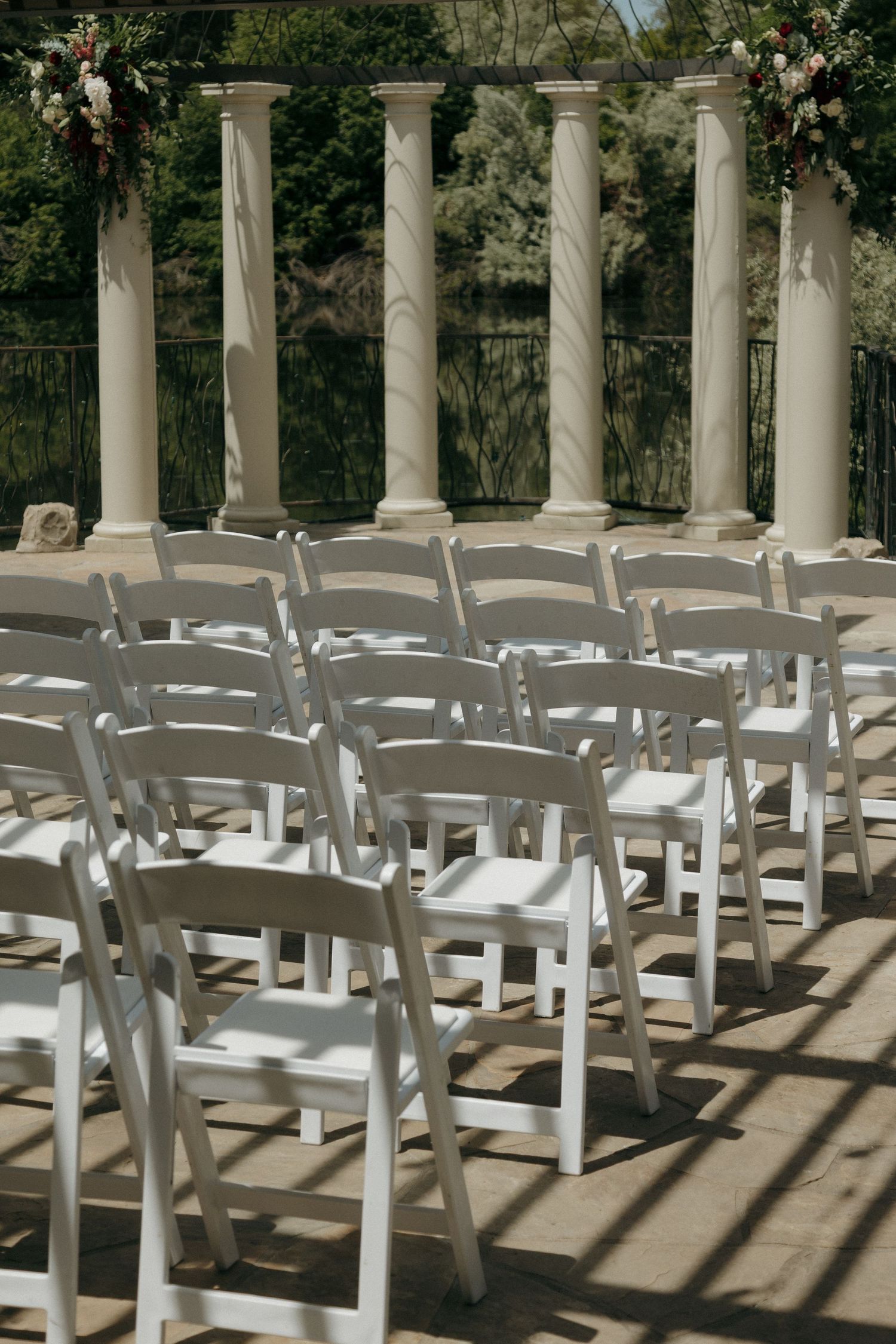 Rows of white folding chairs set up for an outdoor wedding ceremony with elegant white columns.