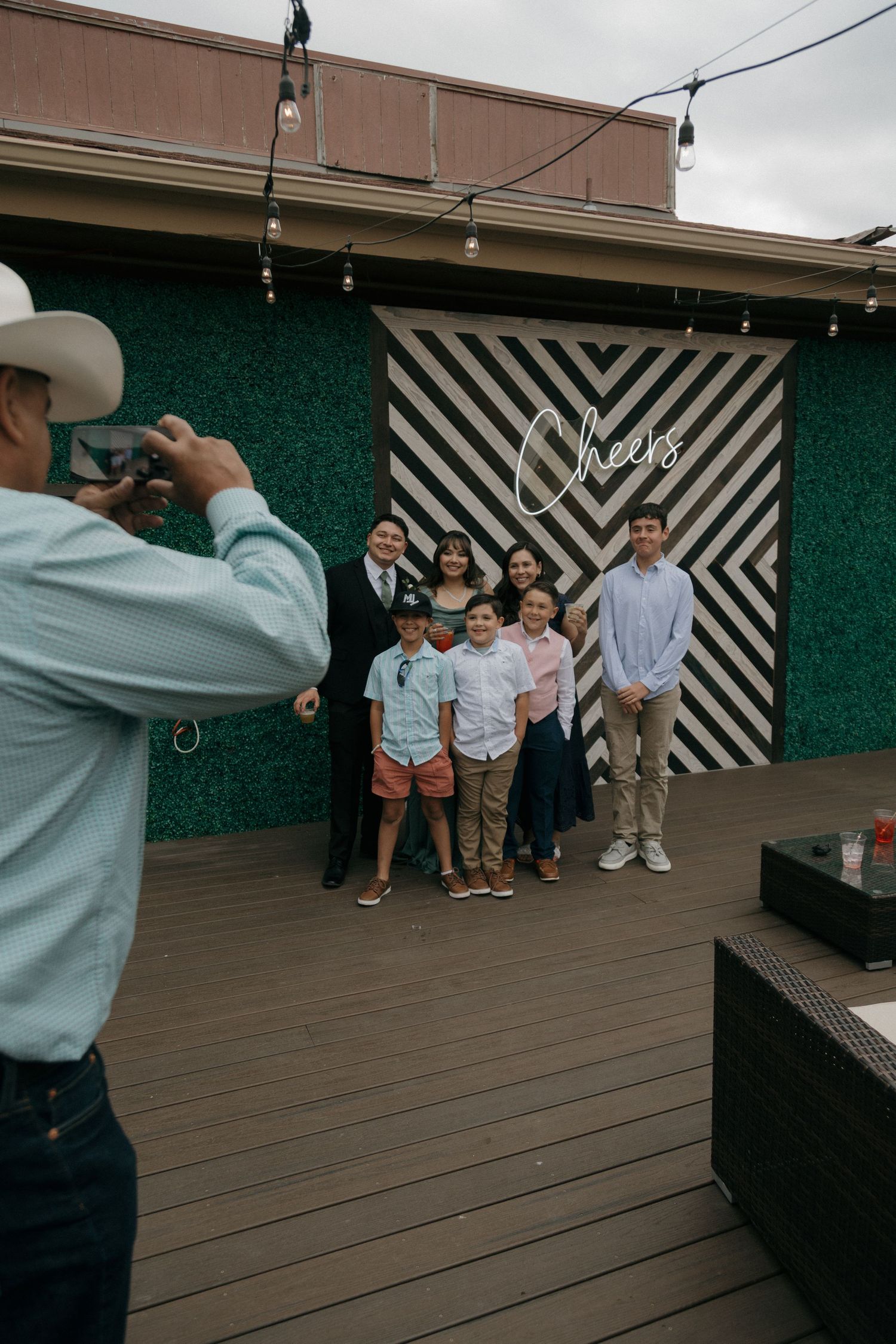 Family group posing for photo in front of striped Cheers backdrop at wedding reception.