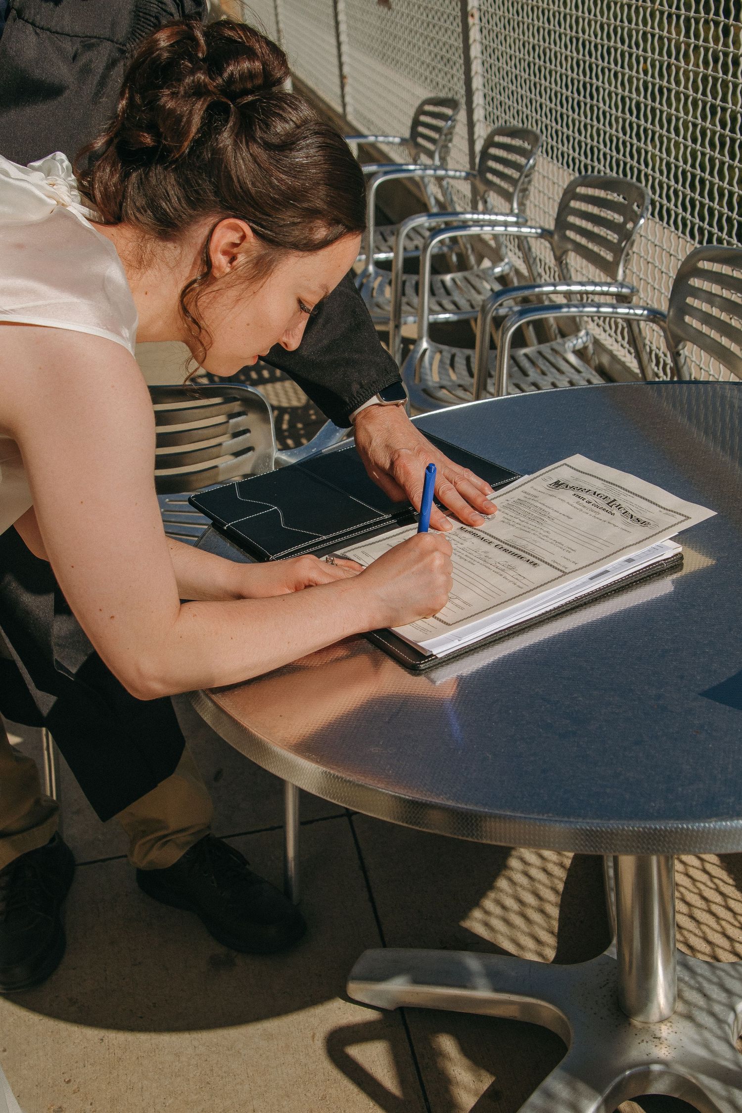 Couple signing marriage documents at a round table on an outdoor terrace.
