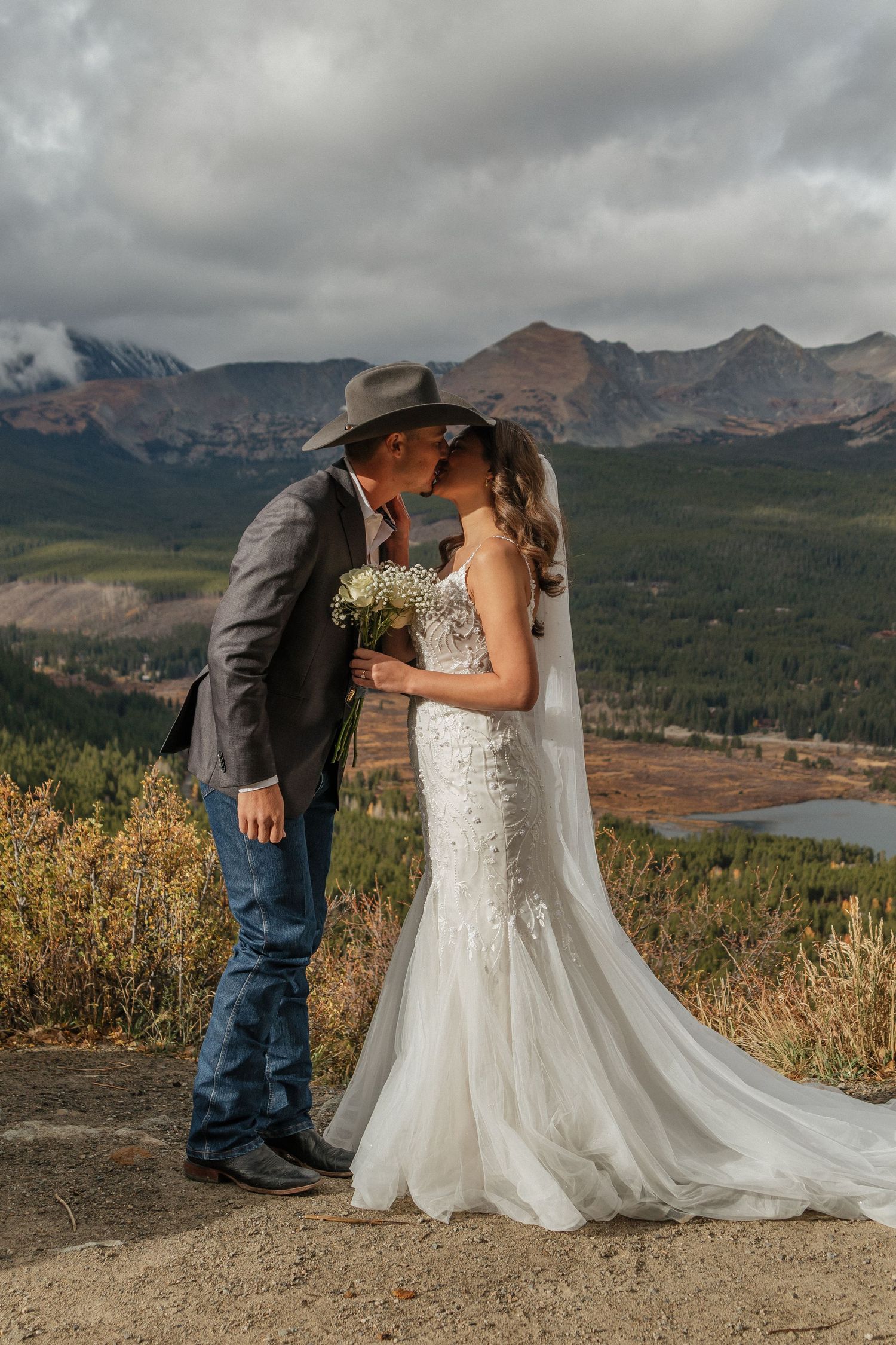 A couple shares a romantic moment against a backdrop of mountains and autumn foliage during their wedding photoshoot.