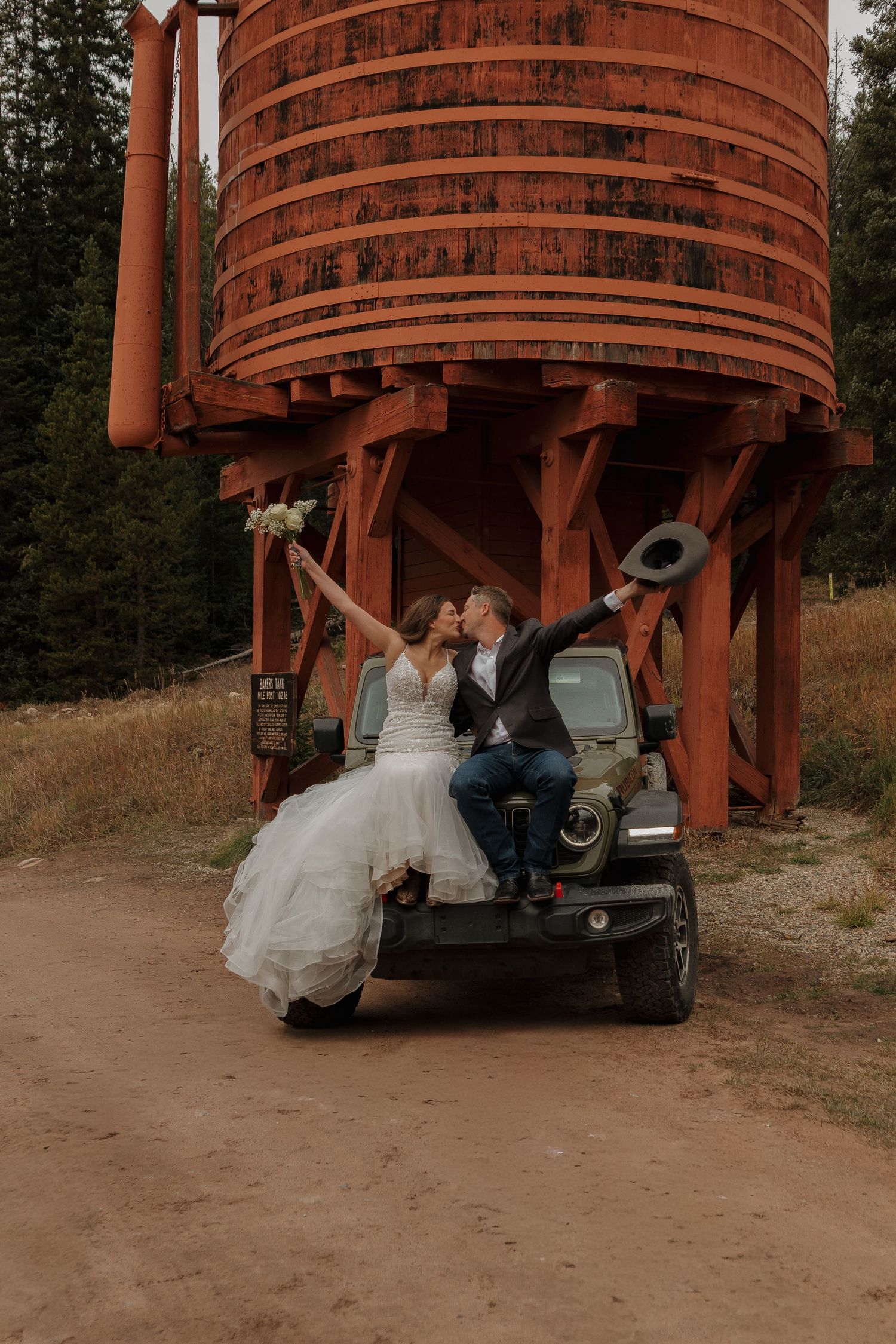 Newlyweds pose beneath a rustic wooden water tower structure at sunset.