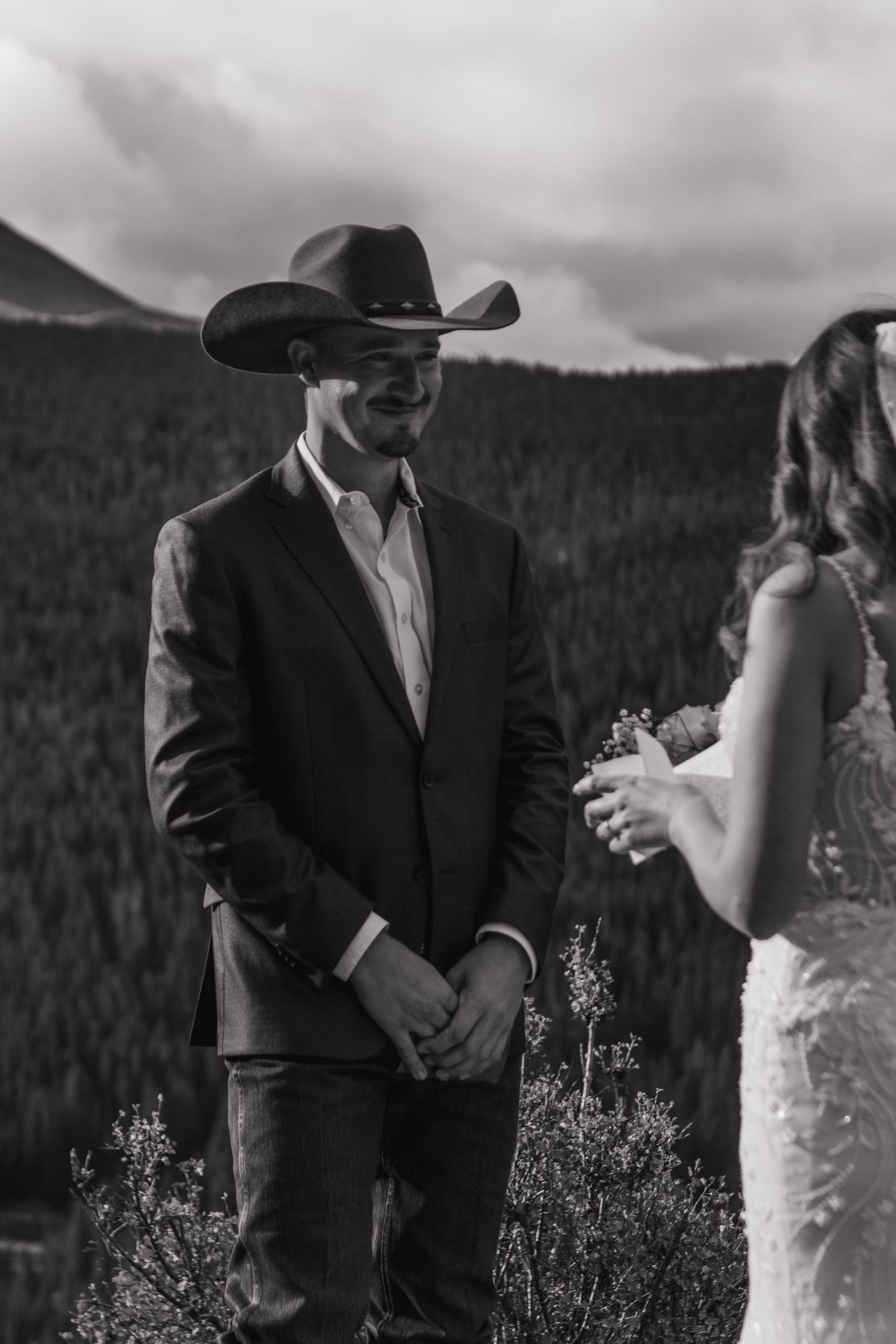 A western wedding couple shares a moment on a mountainside with evergreen forests in the background.