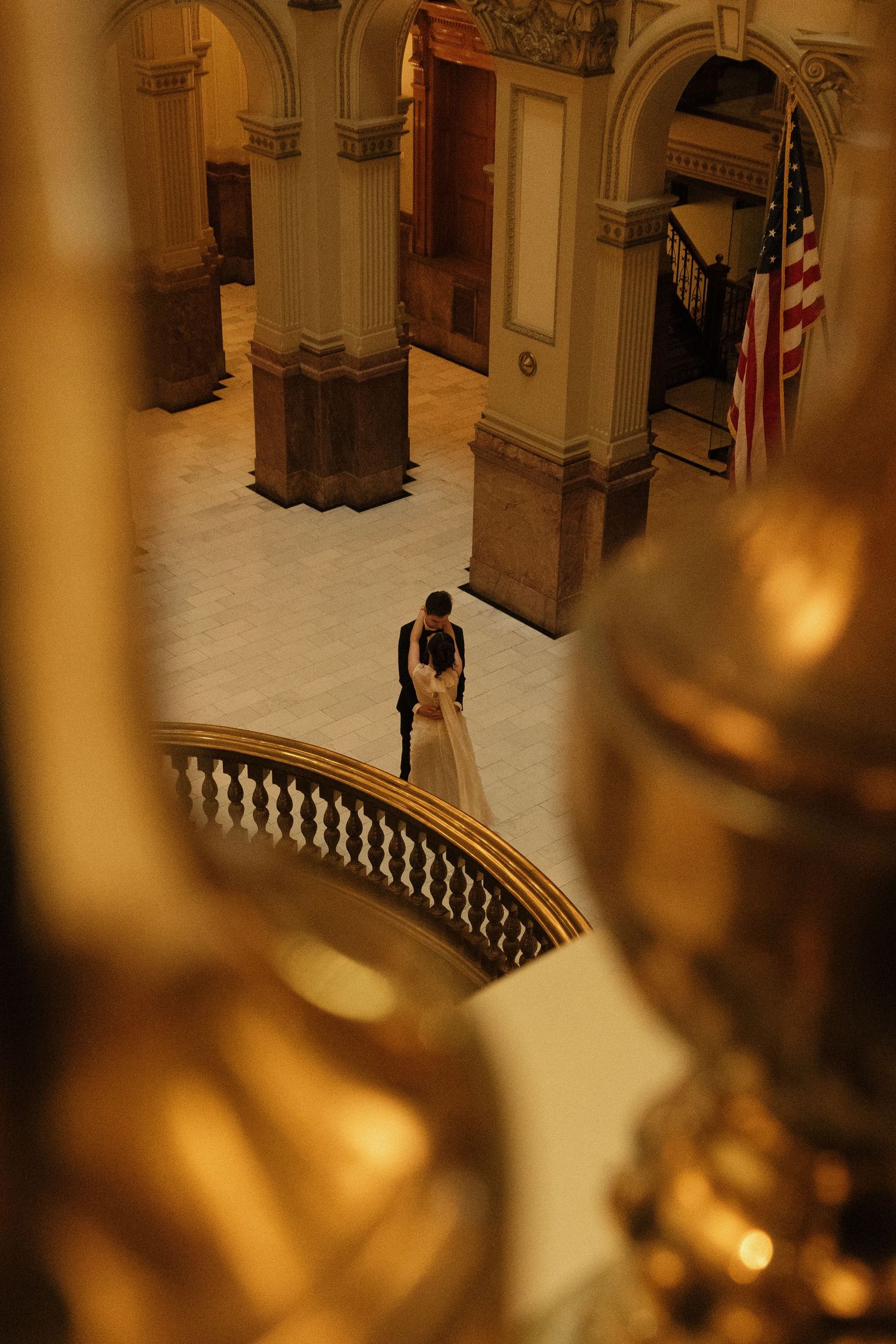 An ornate interior hallway with curved balustrades and arches cast in warm golden lighting.
