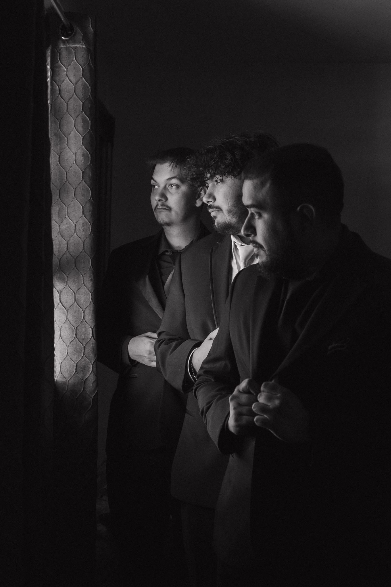 Dark moody black and white portrait sequence showing two figures in suits standing against a wall in low light.