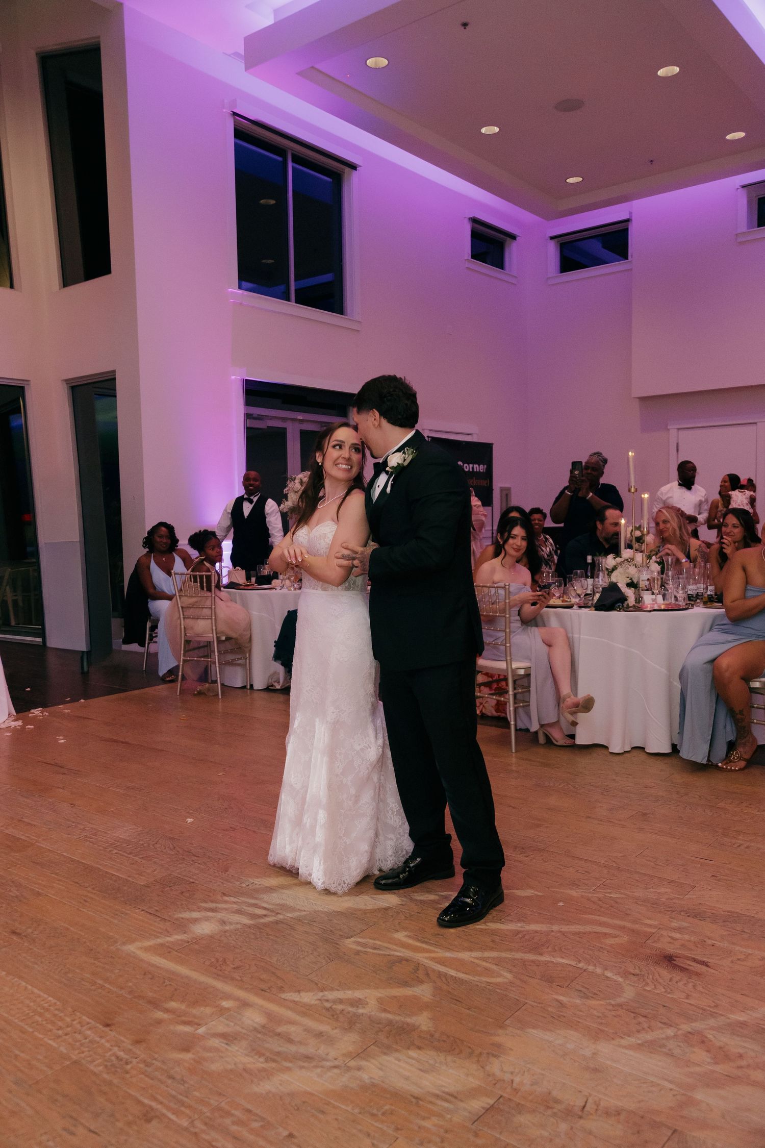 Bride and groom share their first dance in an elegant wedding reception hall with purple uplighting.