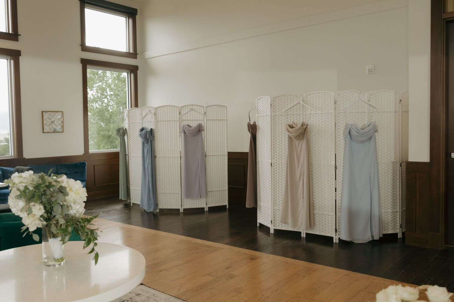 Bridesmaid dresses in blue and neutral tones displayed on white decorative room dividers indoors.