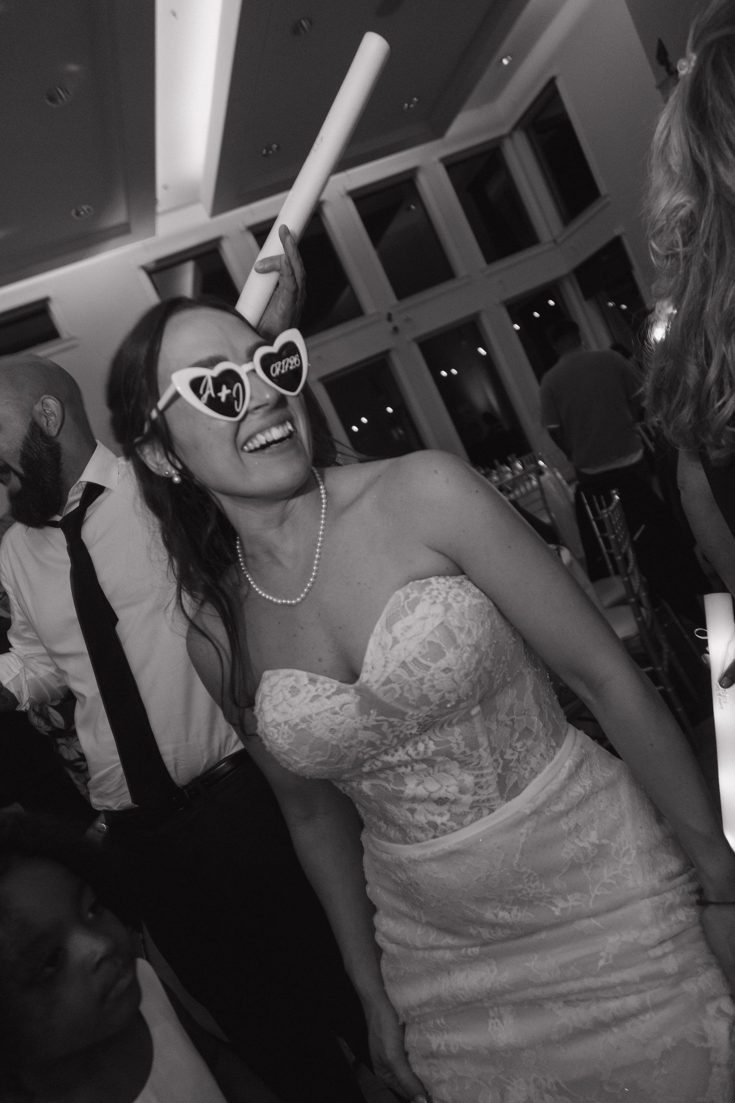 Bride dancing at wedding reception in black and white photo wearing heart-shaped bridal sunglasses.