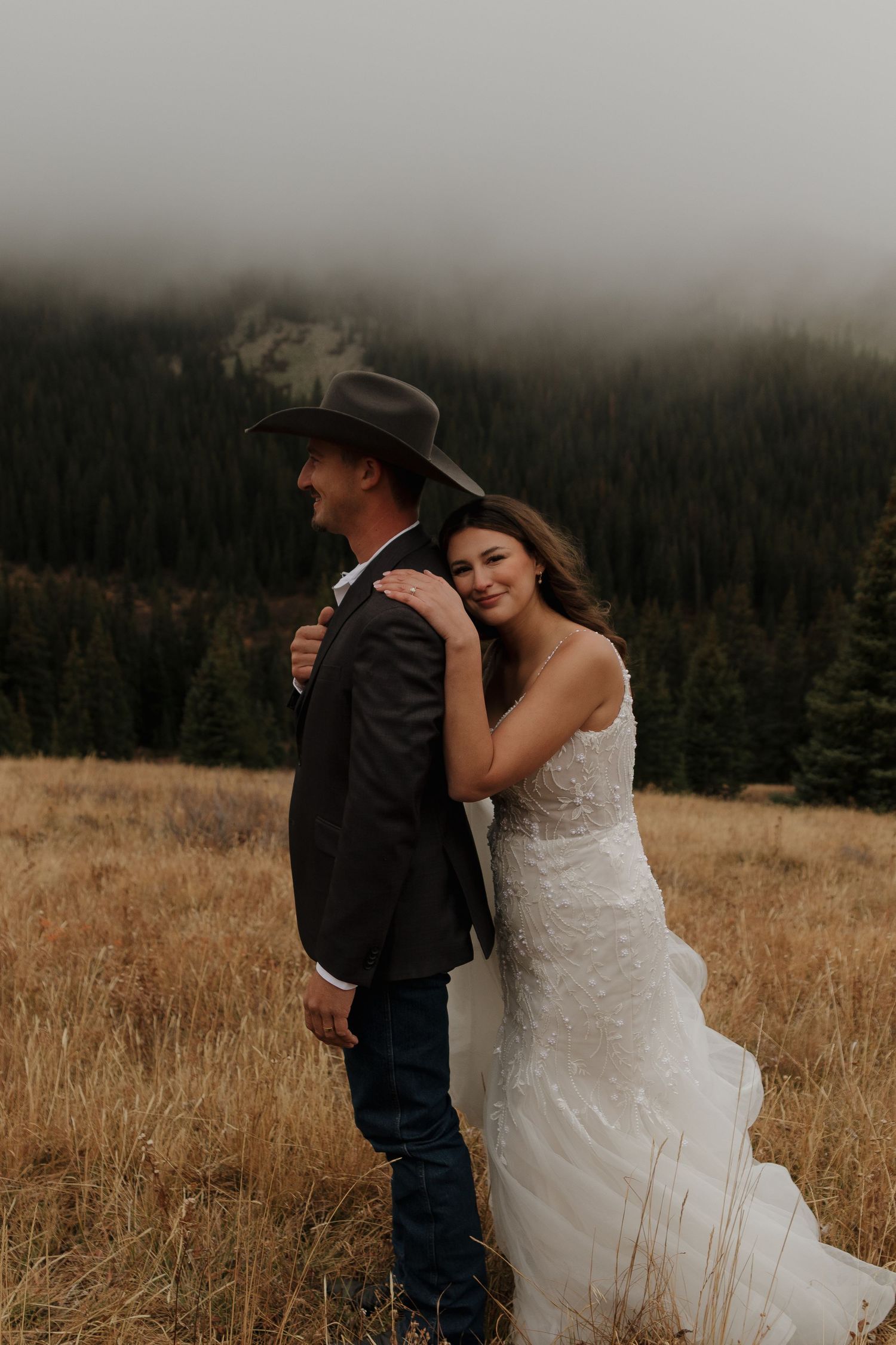A western-themed wedding couple embraces in a mountain meadow.