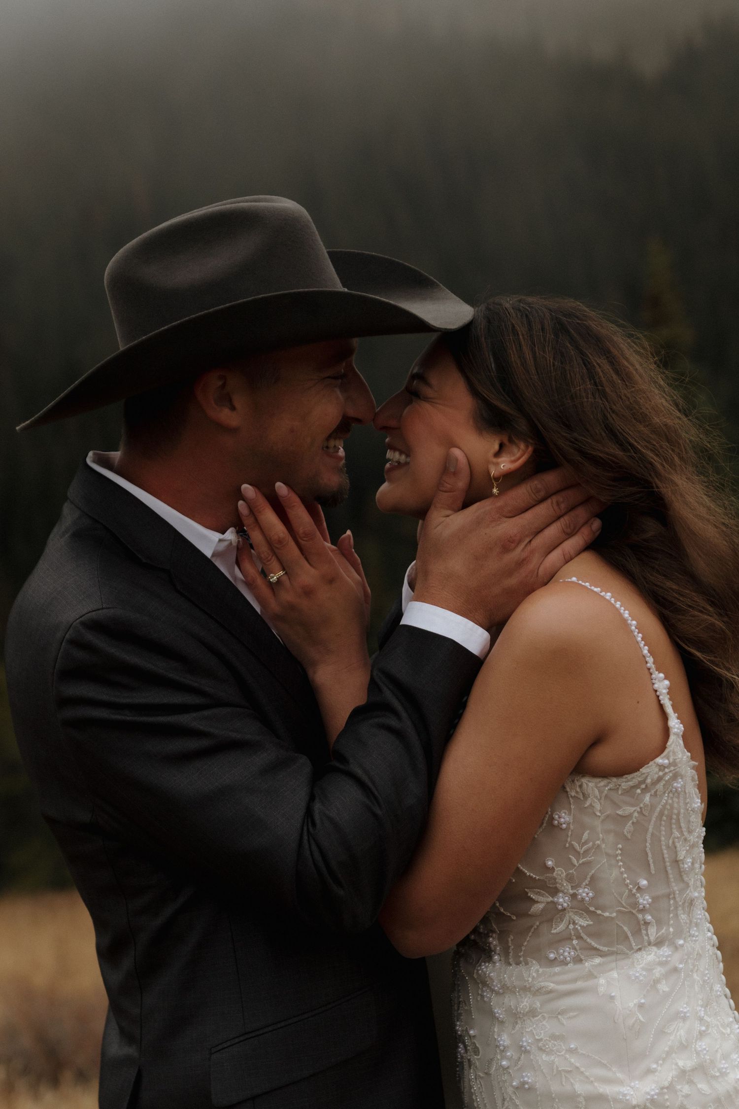 An intimate moment between newlyweds with a black cowboy hat against a moody mountain landscape.
