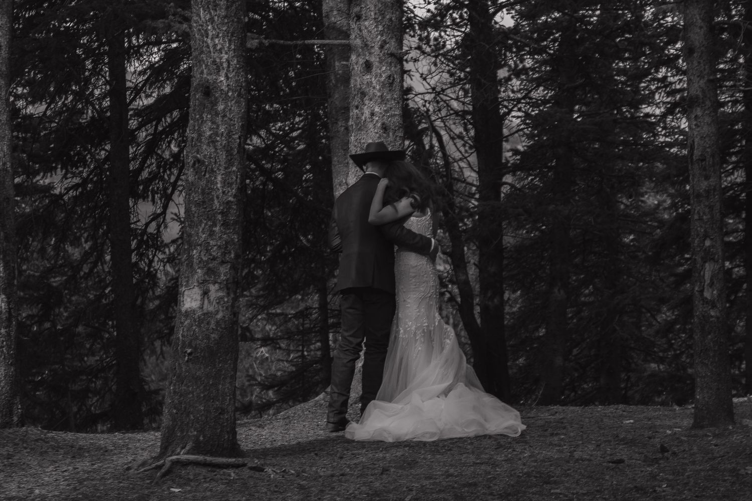 A black and white photo captures a romantic moment between newlyweds in a forest setting.