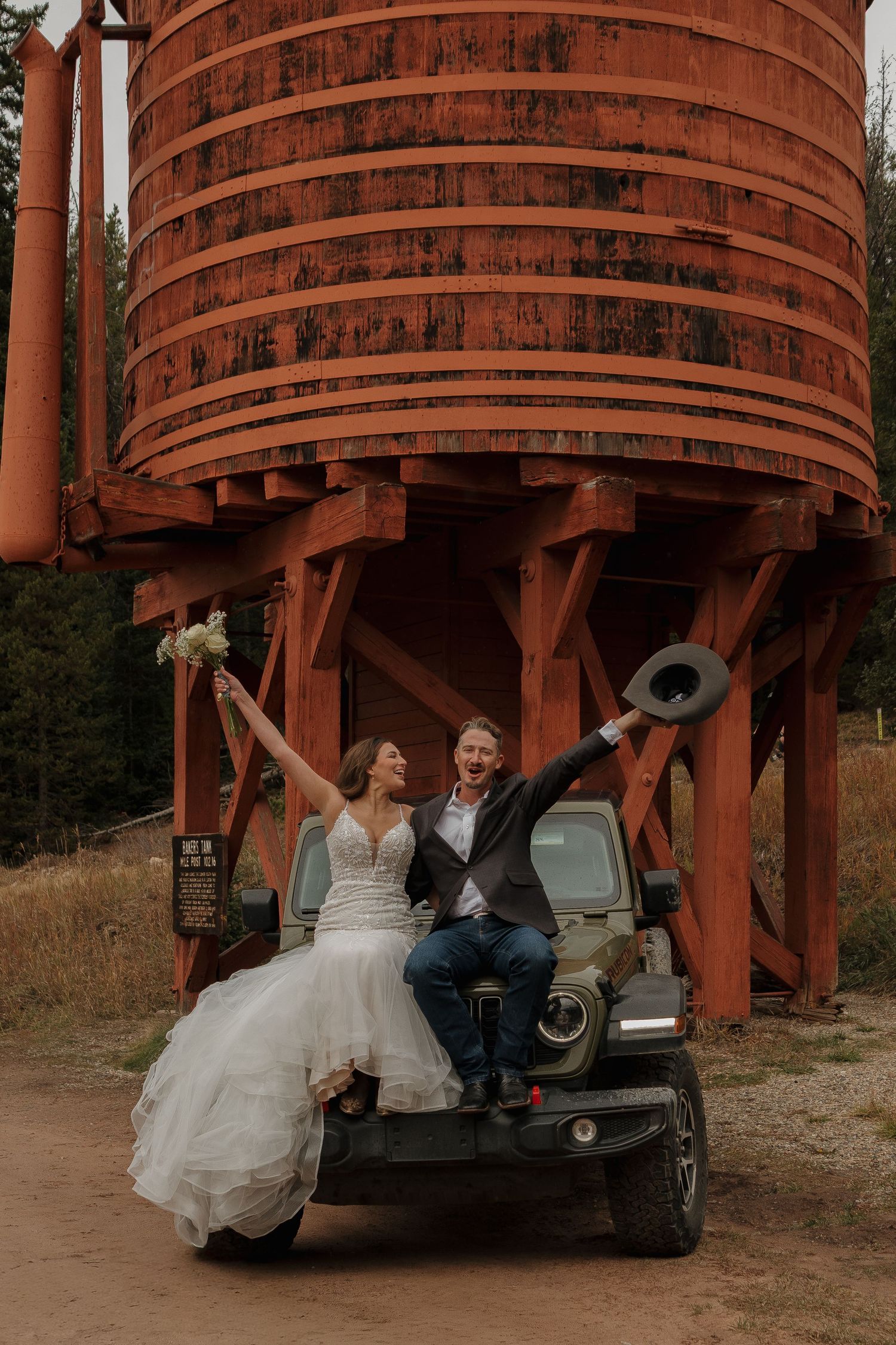 A wedding couple poses playfully beneath large rustic wooden water towers.