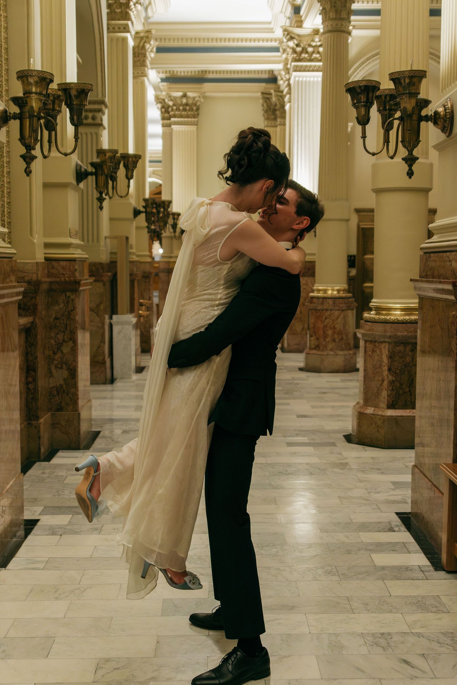 Wedding couple dancing in an ornate marble hallway with classical columns.