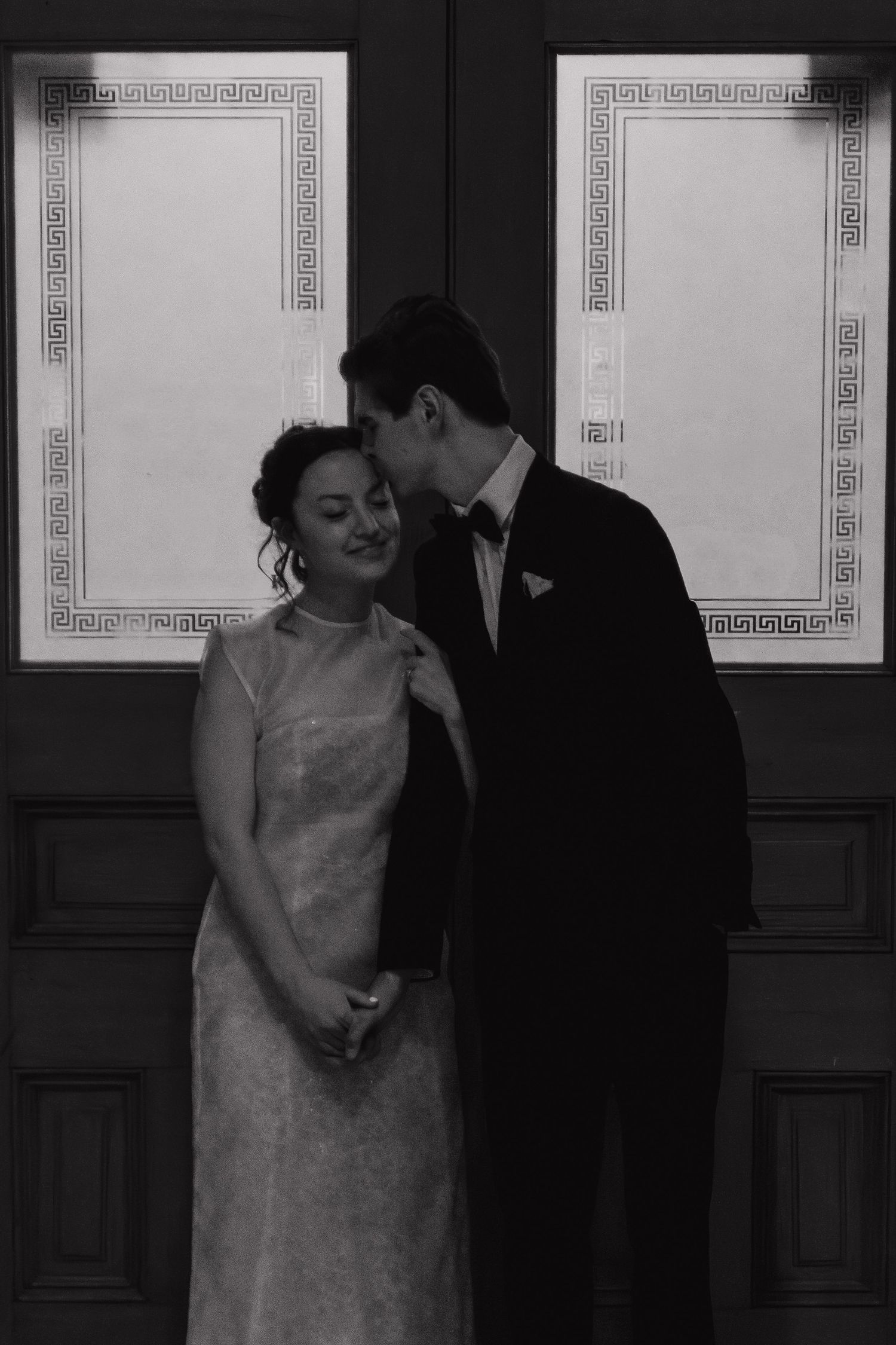 An intimate black and white portrait of newlyweds against a decorative paneled wall.