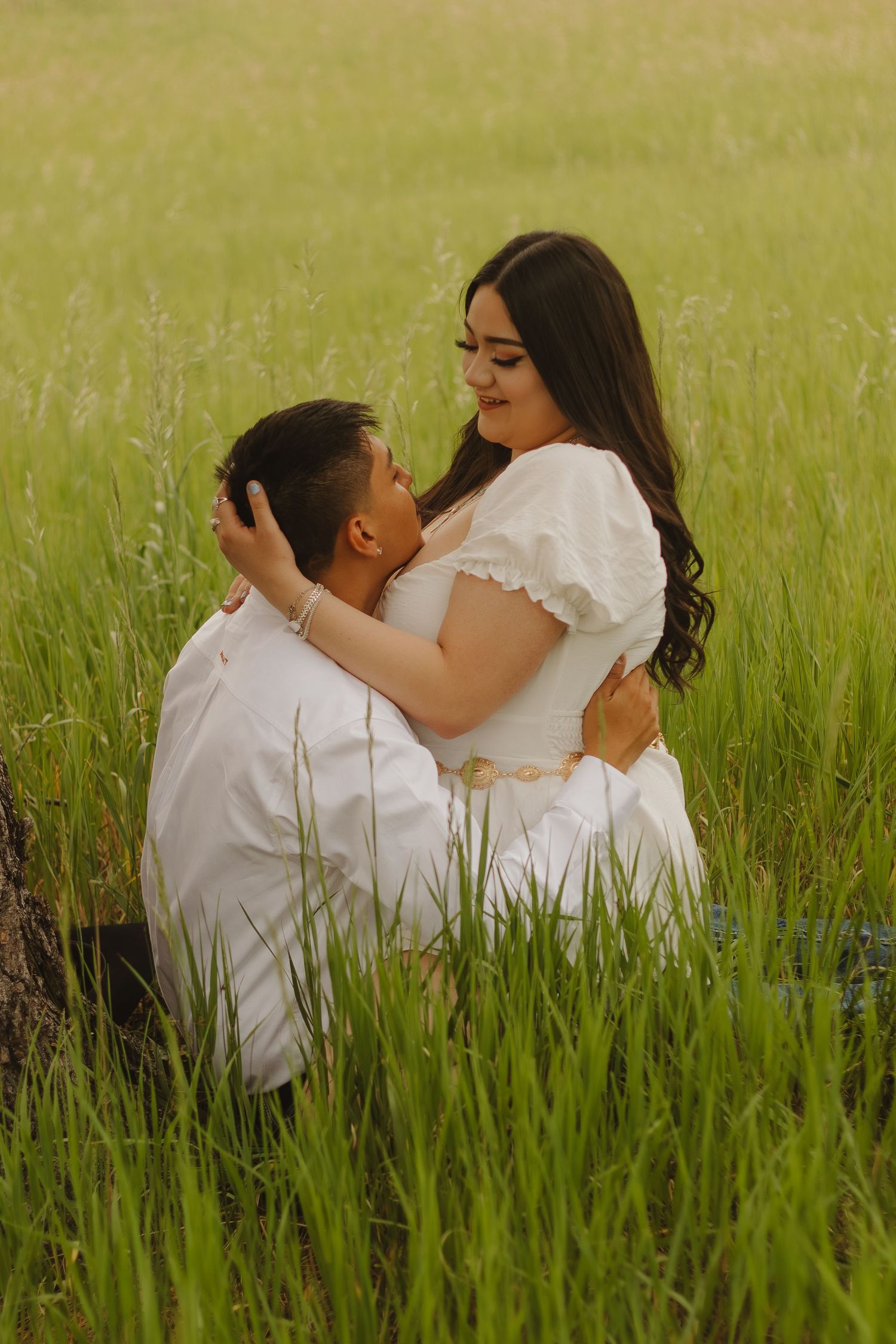 Intimate portrait of a couple embracing in tall grass during a golden hour photoshoot.