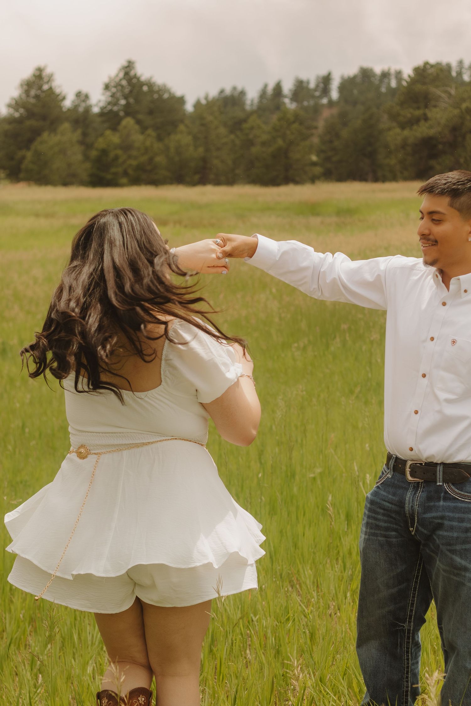 Couple dancing playfully in a meadow, with the woman's white dress twirling.