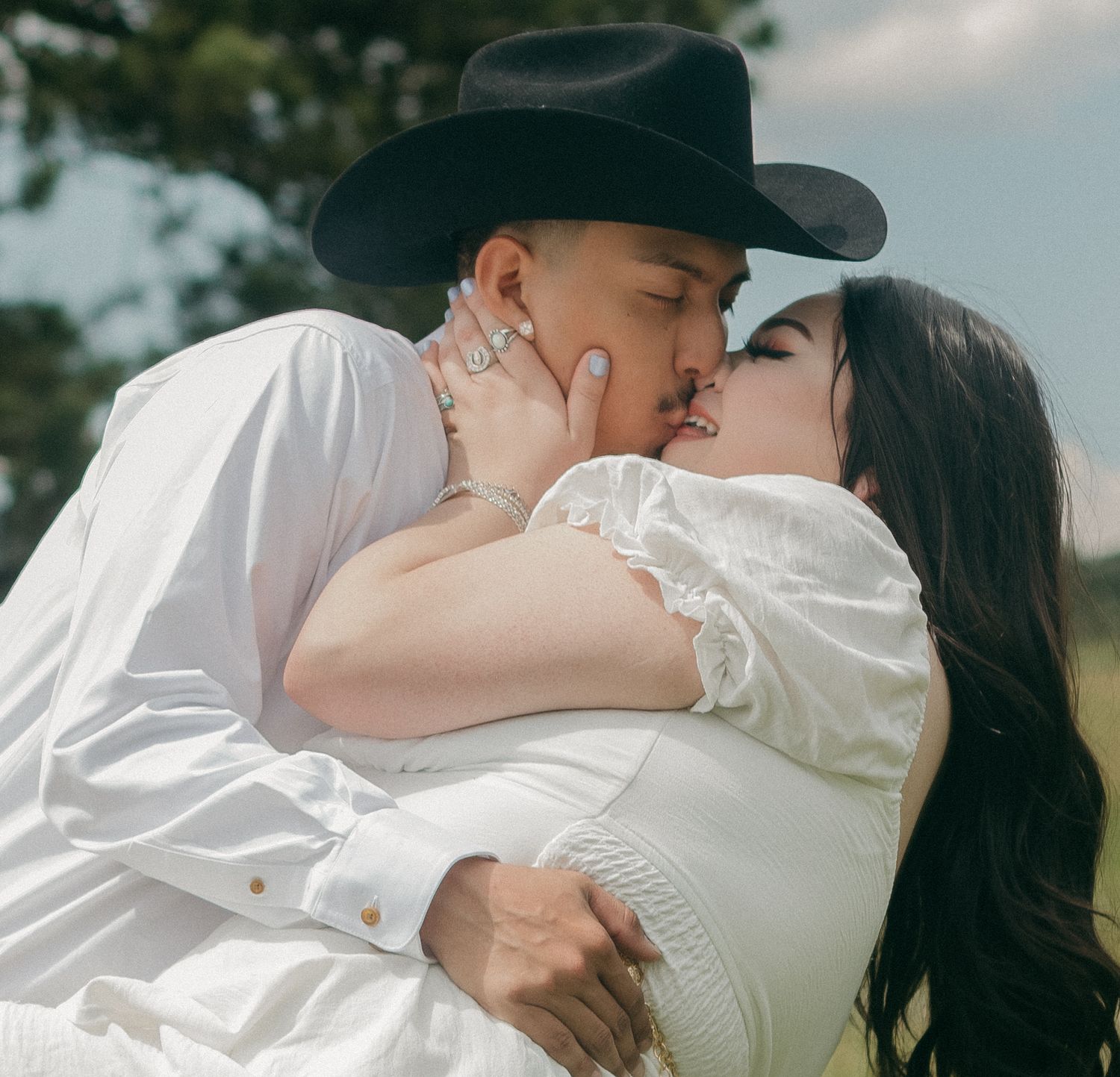 Romantic moment between couple in western wear embracing in a sunny mountain field.