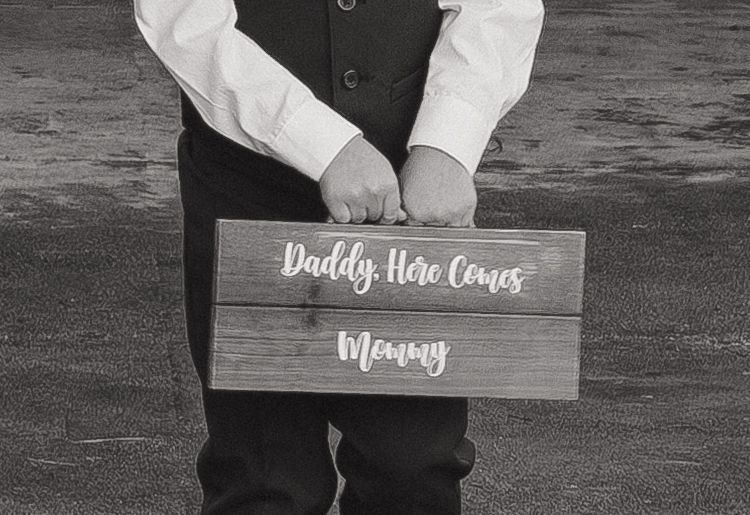 A wooden sign with text is held during a wedding ceremony.
