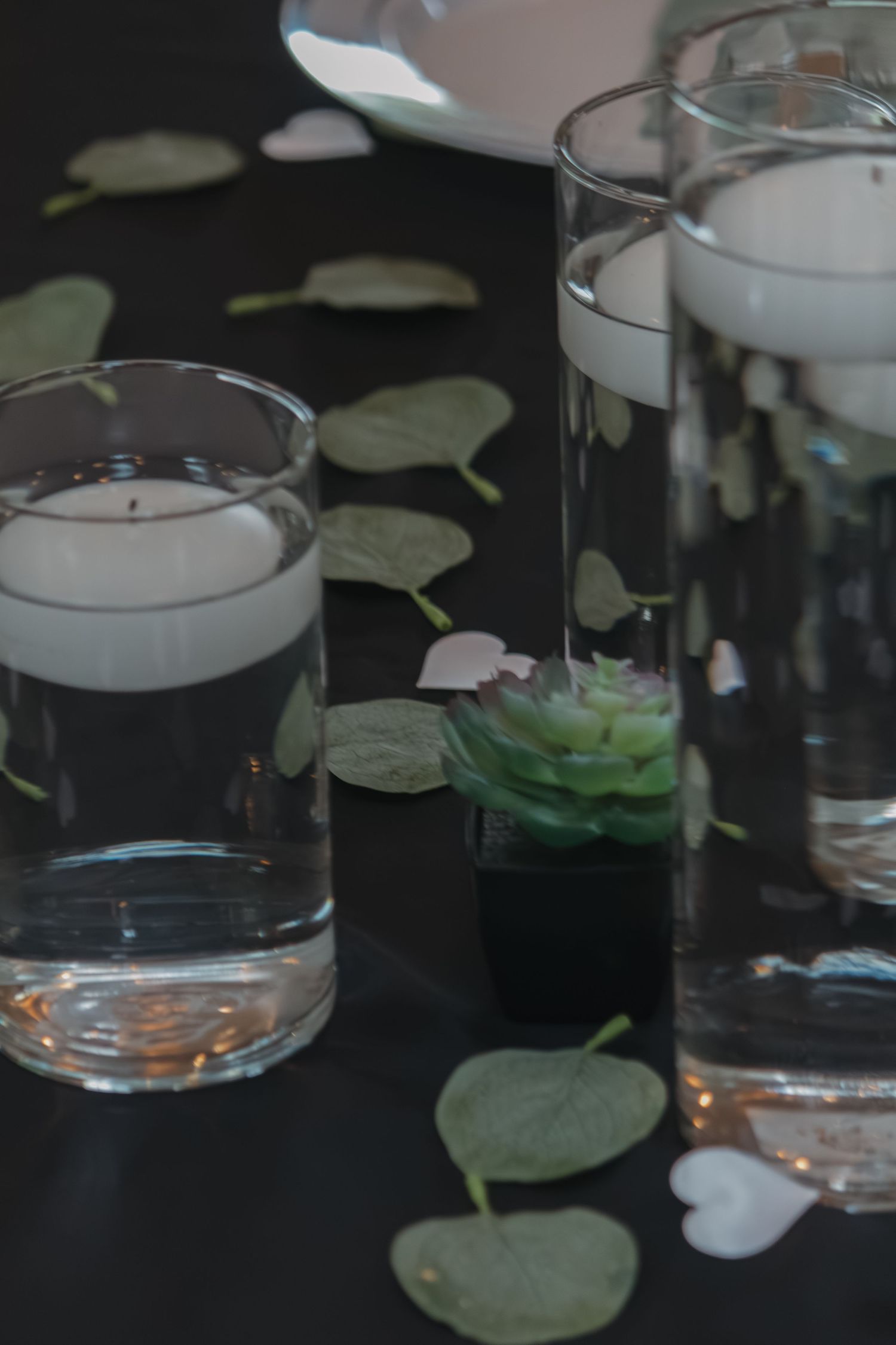 Glass candle holders with water and floating leaves on dark surface.