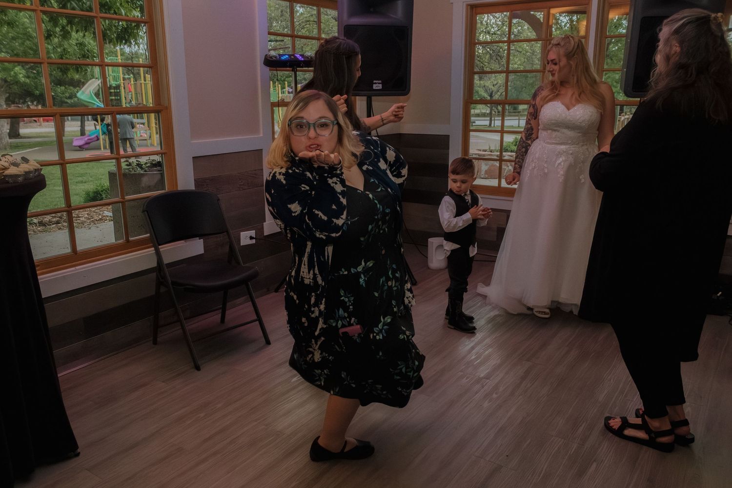 Party guests dance and celebrate on a wooden floor near large windows.