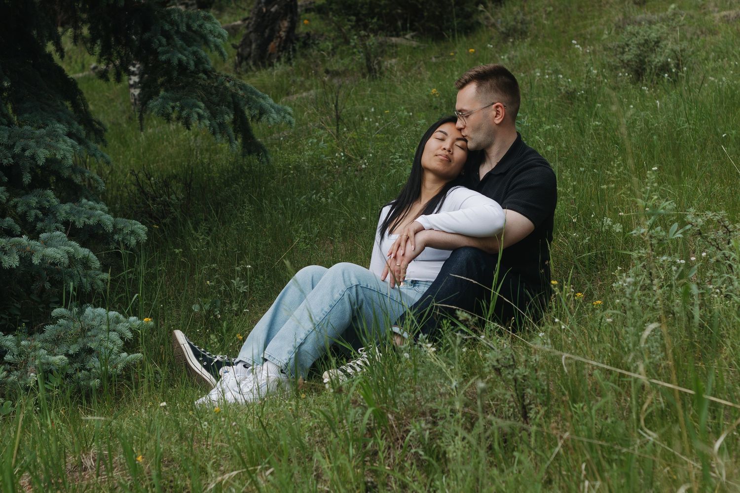 A couple relaxes together in tall grass on a hillside.